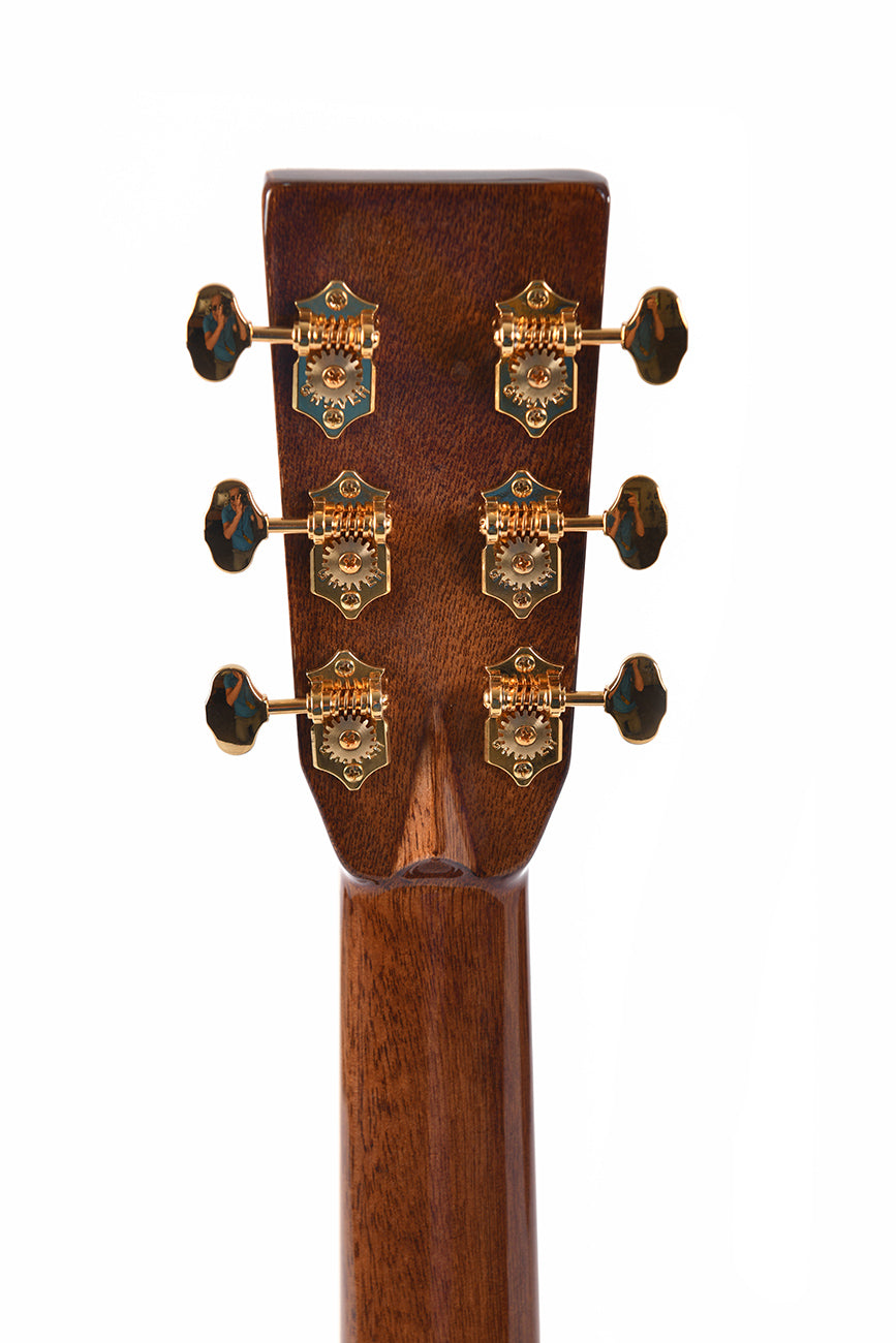 Rear view of an acoustic guitar headstock with six gold tuning machines on a brown wooden neck.
