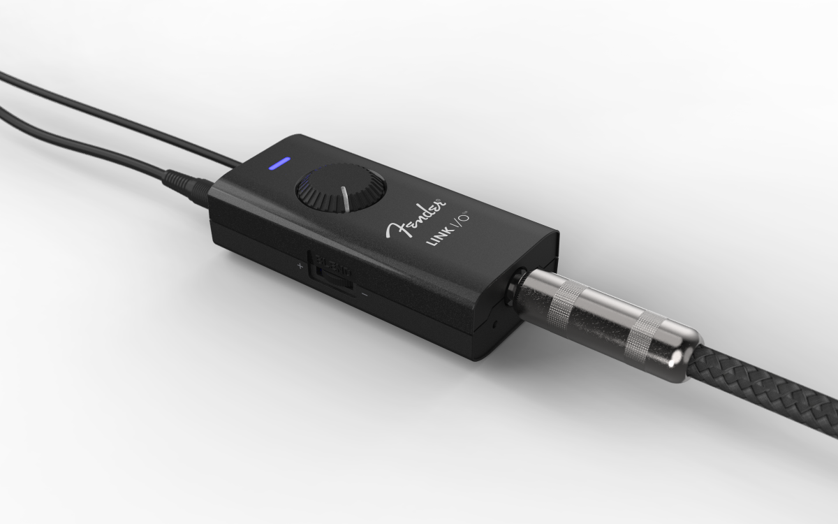Rectangular black Fender Link I/O audio interface with a large top dial, LED indicator, and two cables plugged into opposite ends.