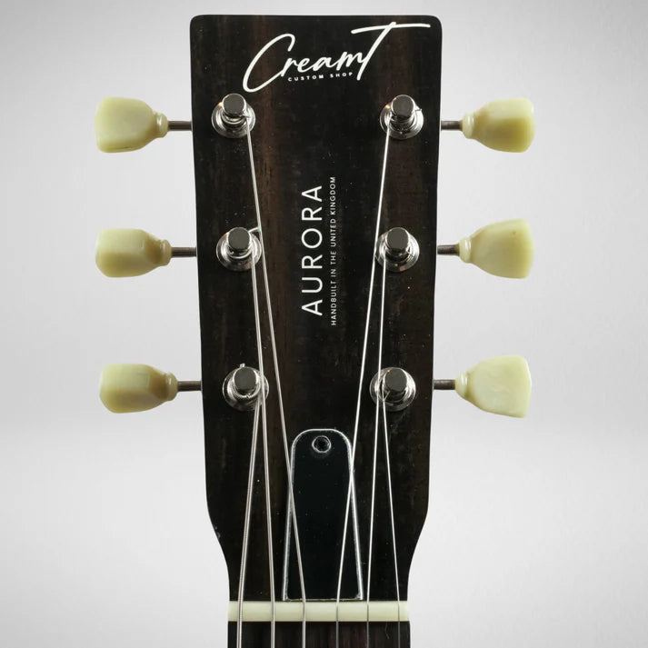 Close-up of a six-string electric guitar headstock labeled Aurora by Cream T Custom Shop, showing tuning pegs and strings.