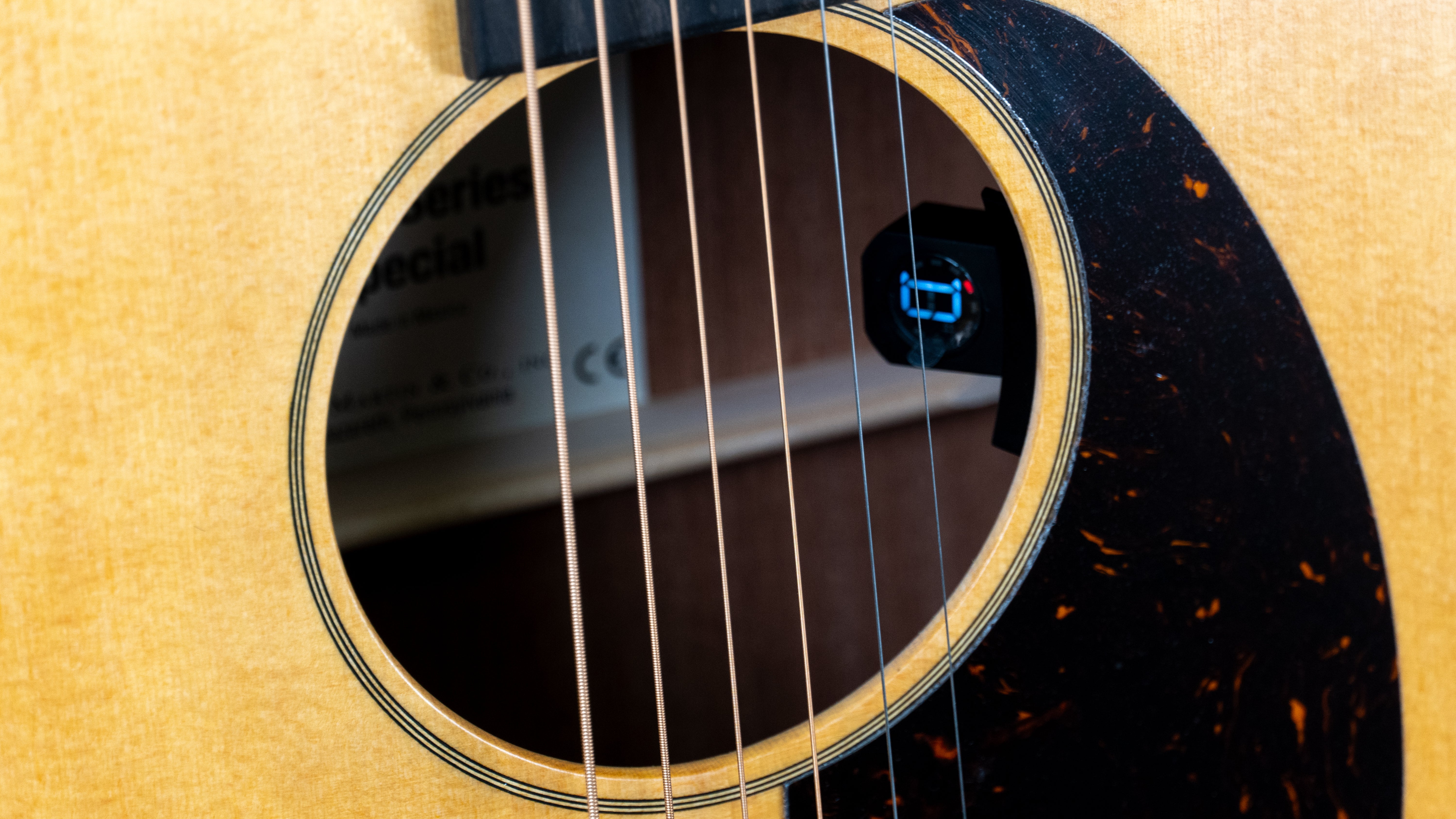 Close-up of an acoustic guitar soundhole with six strings and an electronic tuner clipped inside the soundhole.