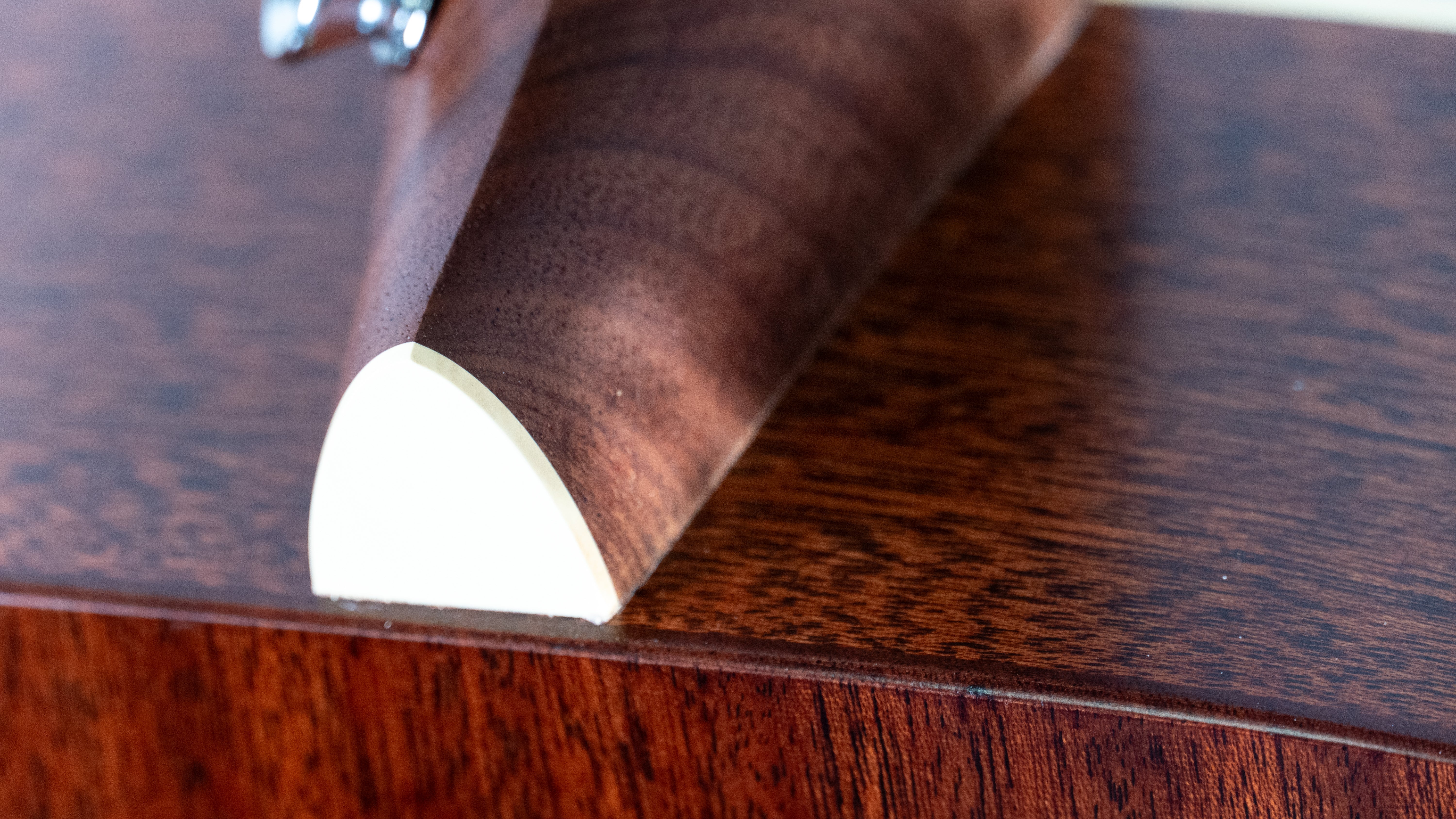 Close-up of an acoustic guitar neck joint showing the glossy wood finish and cream-colored heel cap detail.
