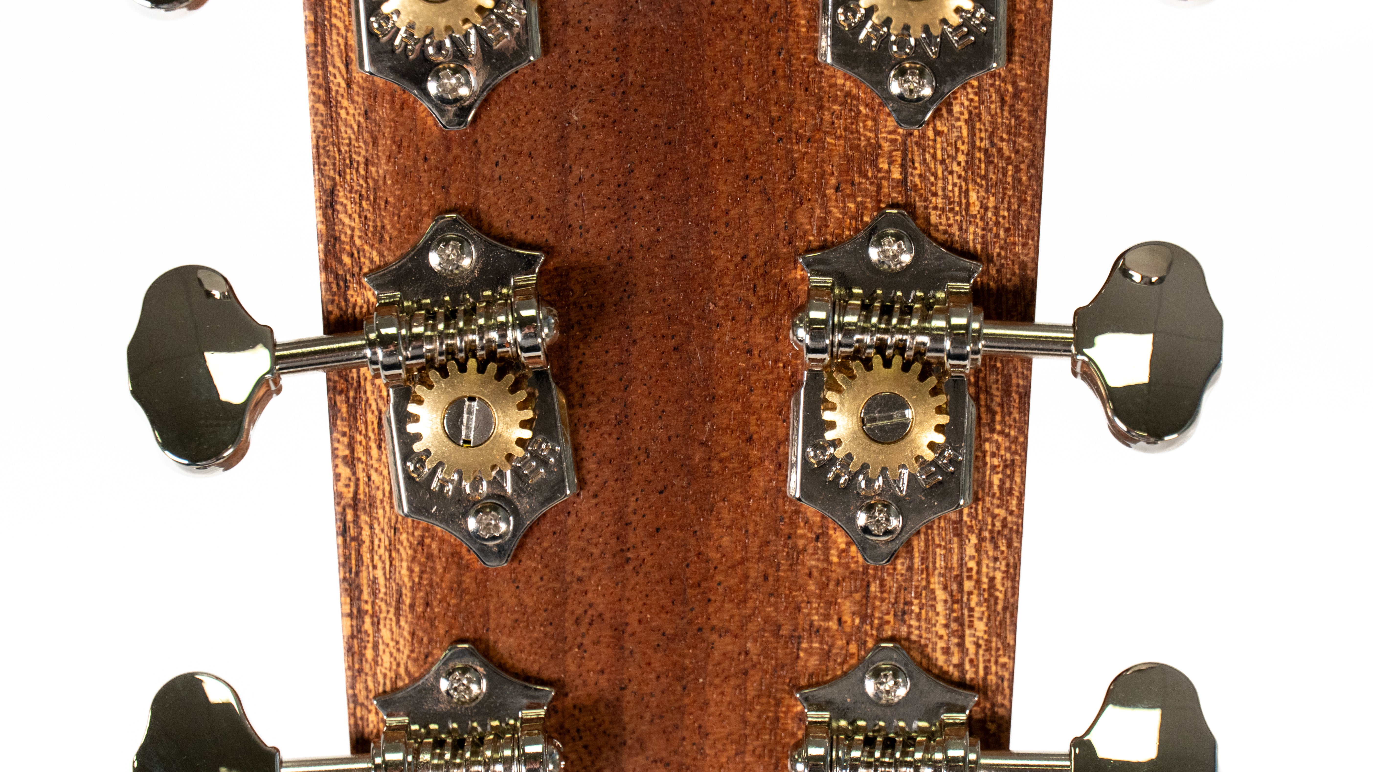 Close-up of an acoustic guitar’s headstock showing three pairs of shiny metal tuning machines with exposed brass gears on a wood surface.