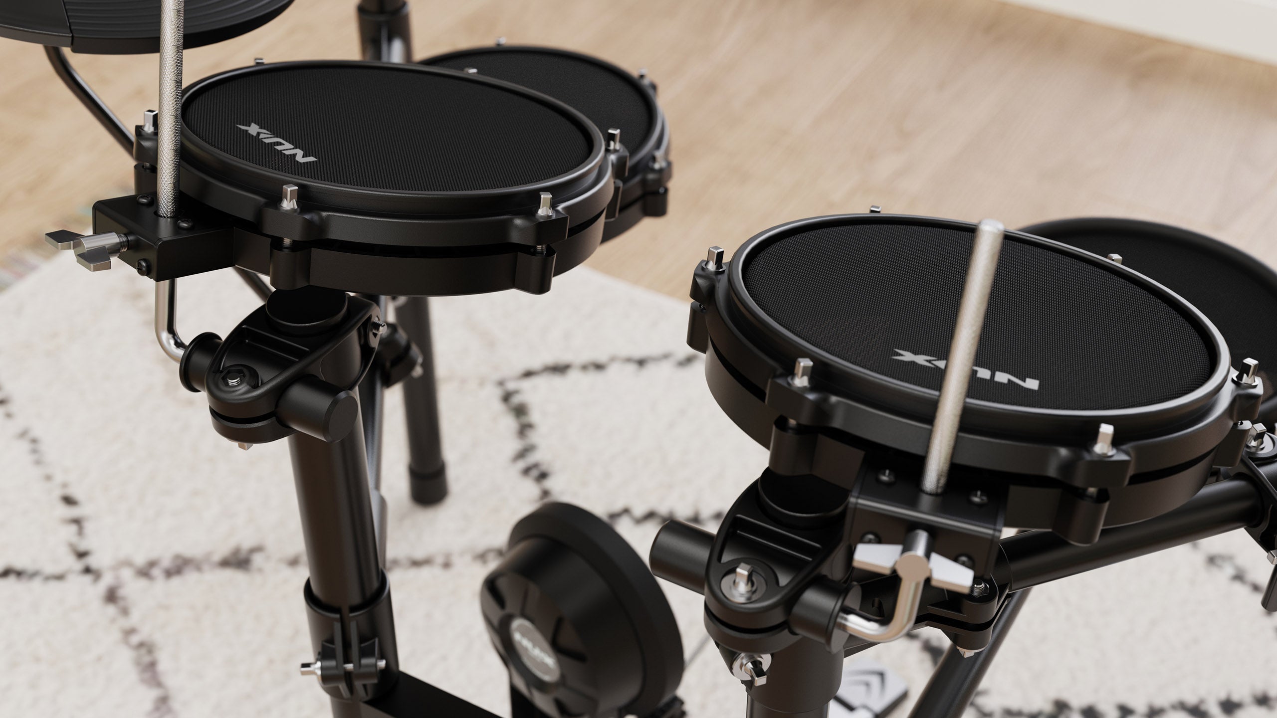 Close-up of black NUX electronic drum pads with mesh heads mounted on a metal frame, partially on a light patterned rug and wood floor.