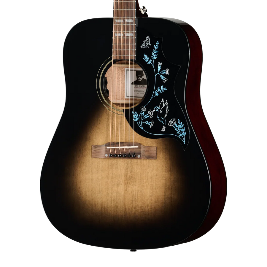 Sunburst-finish acoustic guitar with a black pickguard decorated with light blue outlines of flowers, leaves, a butterfly, and a bird.