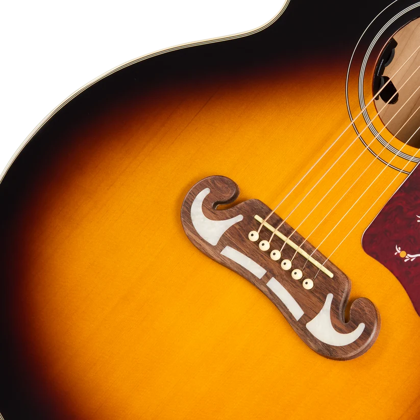 Sunburst acoustic guitar body with a decorative moustache-shaped wooden bridge, six strings, and part of a red floral pickguard visible.