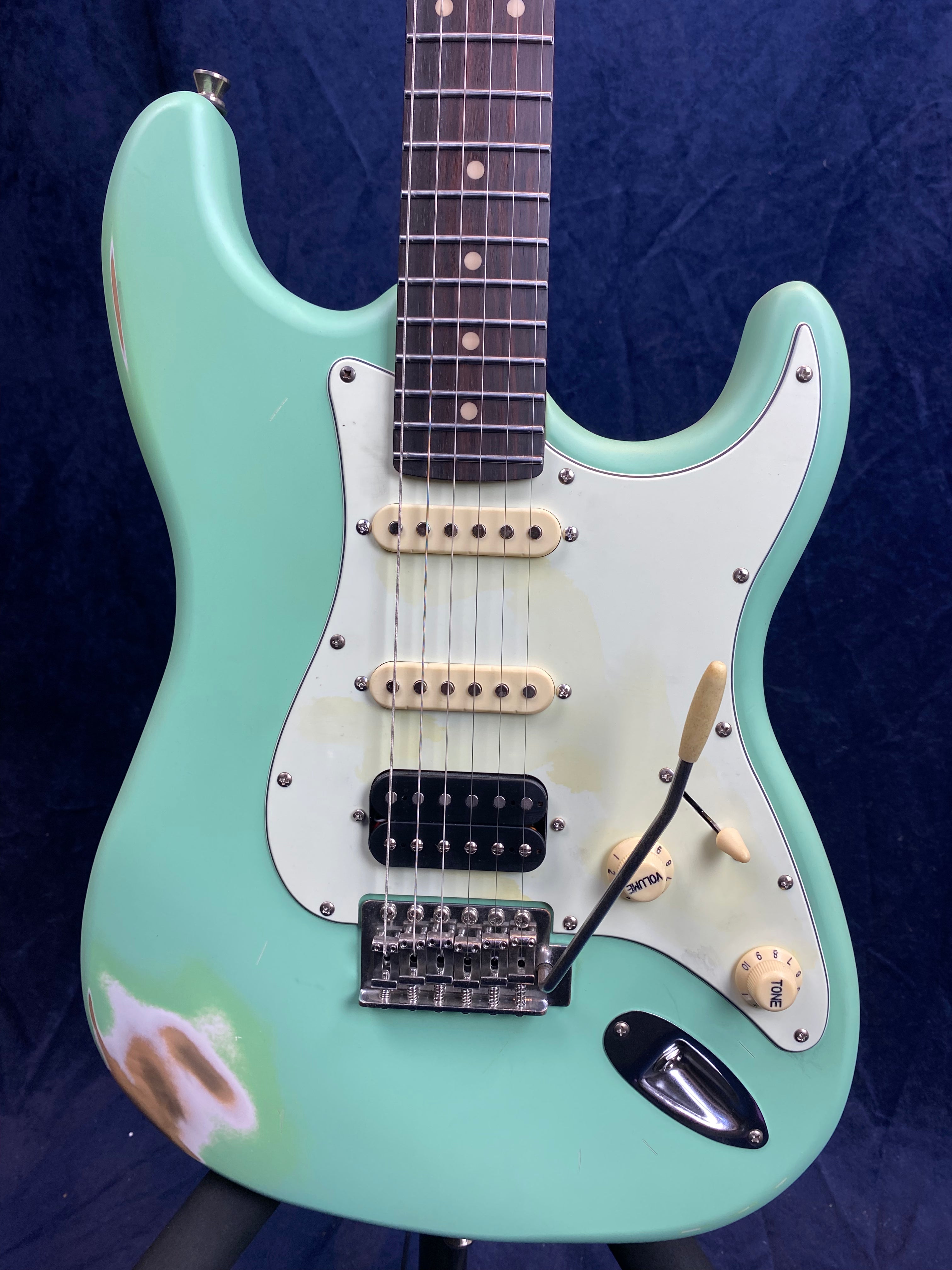 Seafoam green electric guitar with a white pickguard, visible wear near the edge, three pickups, and cream-colored knobs and pickup covers.