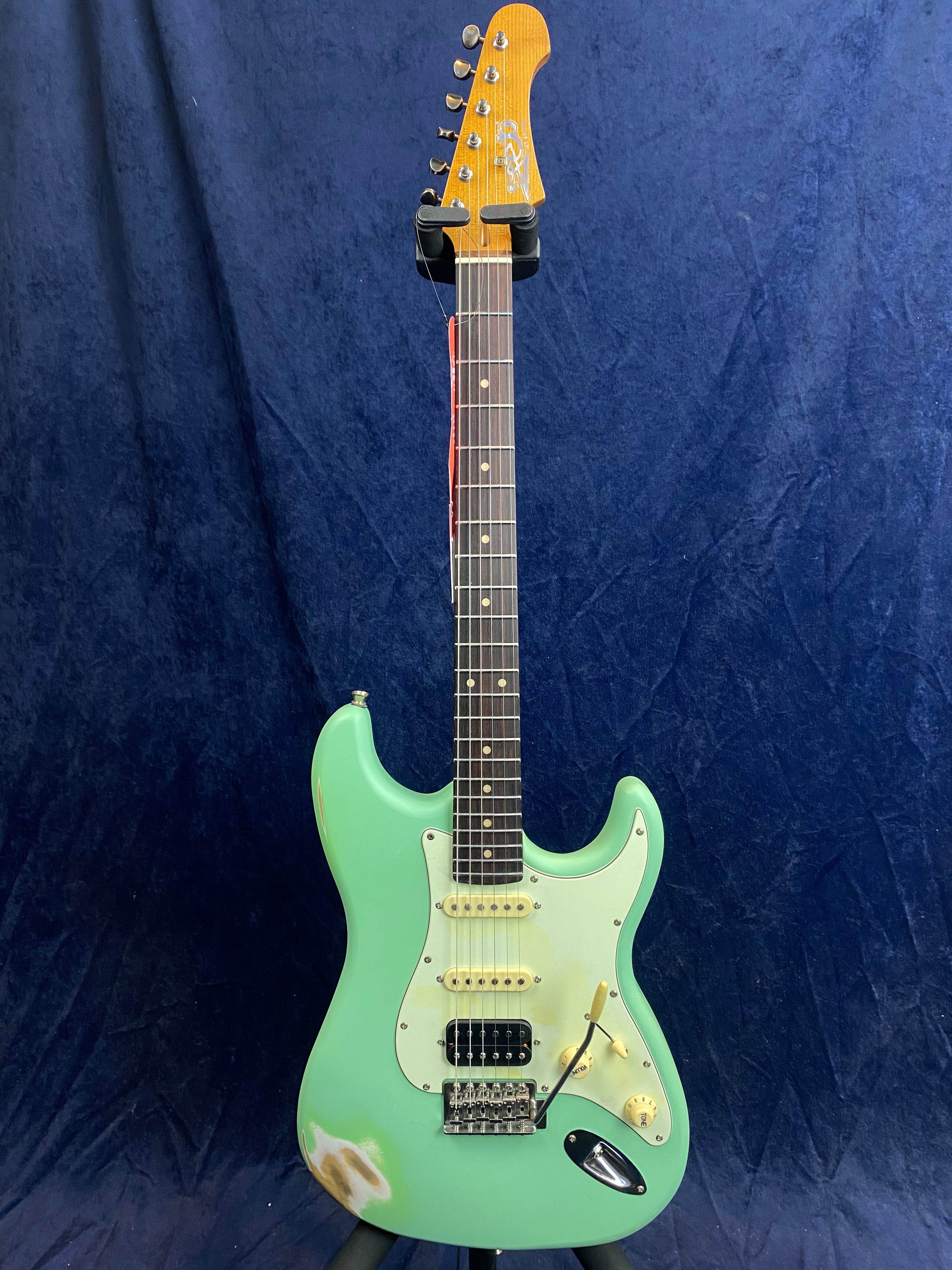 Seafoam green electric guitar with a white pickguard, three pickups, worn paint near the bottom, and a maple headstock against a dark blue background.
