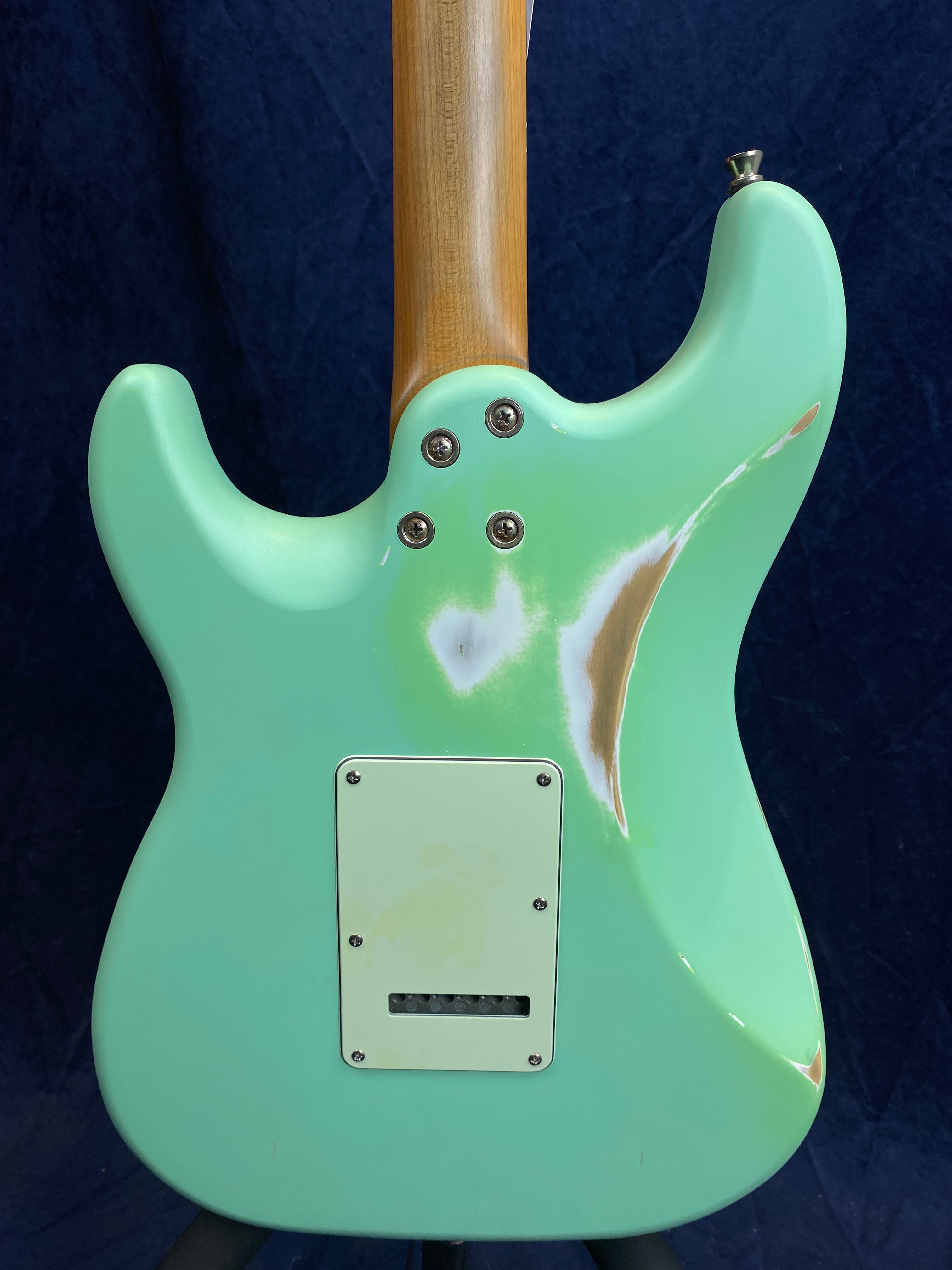 Mint green electric guitar back with visible wood showing through worn paint areas and a rectangular plastic cover plate held by screws.