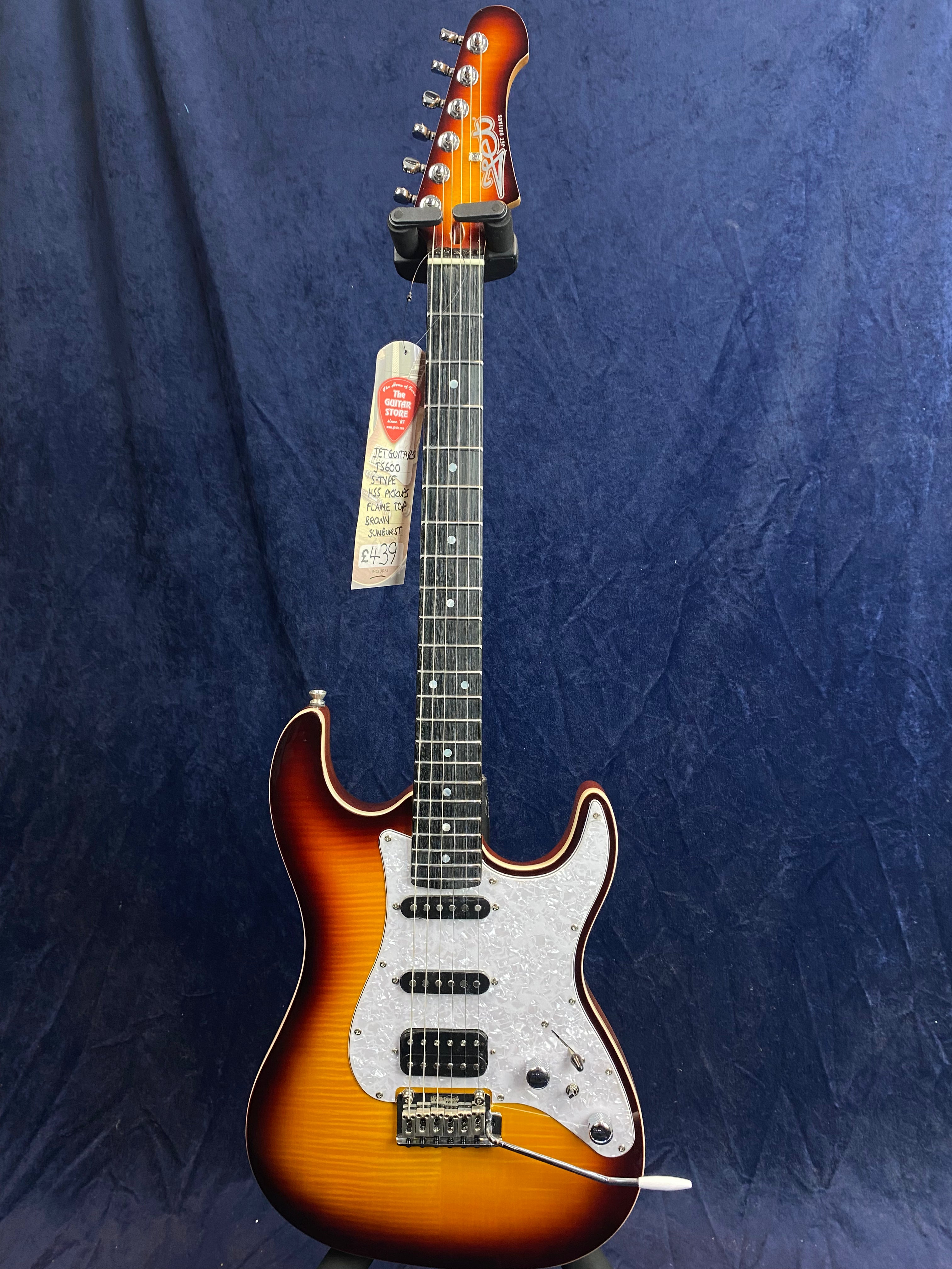 Sunburst electric guitar with a white pearloid pickguard, three pickups, and a tremolo bridge, hanging against a dark blue background.