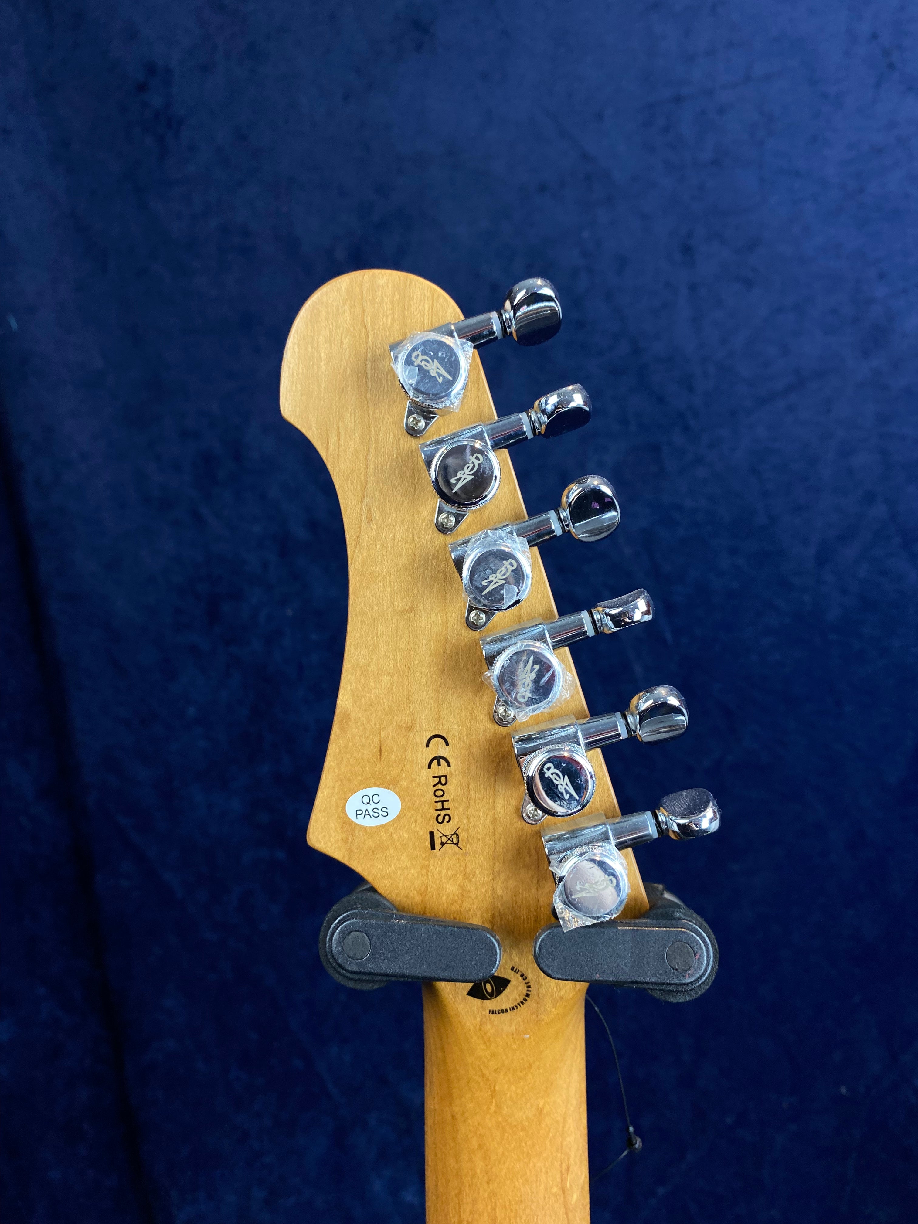 Six chrome tuning pegs line the back of a light wooden electric guitar headstock marked with QC PASS, CE, and RoHS labels against a dark blue background.