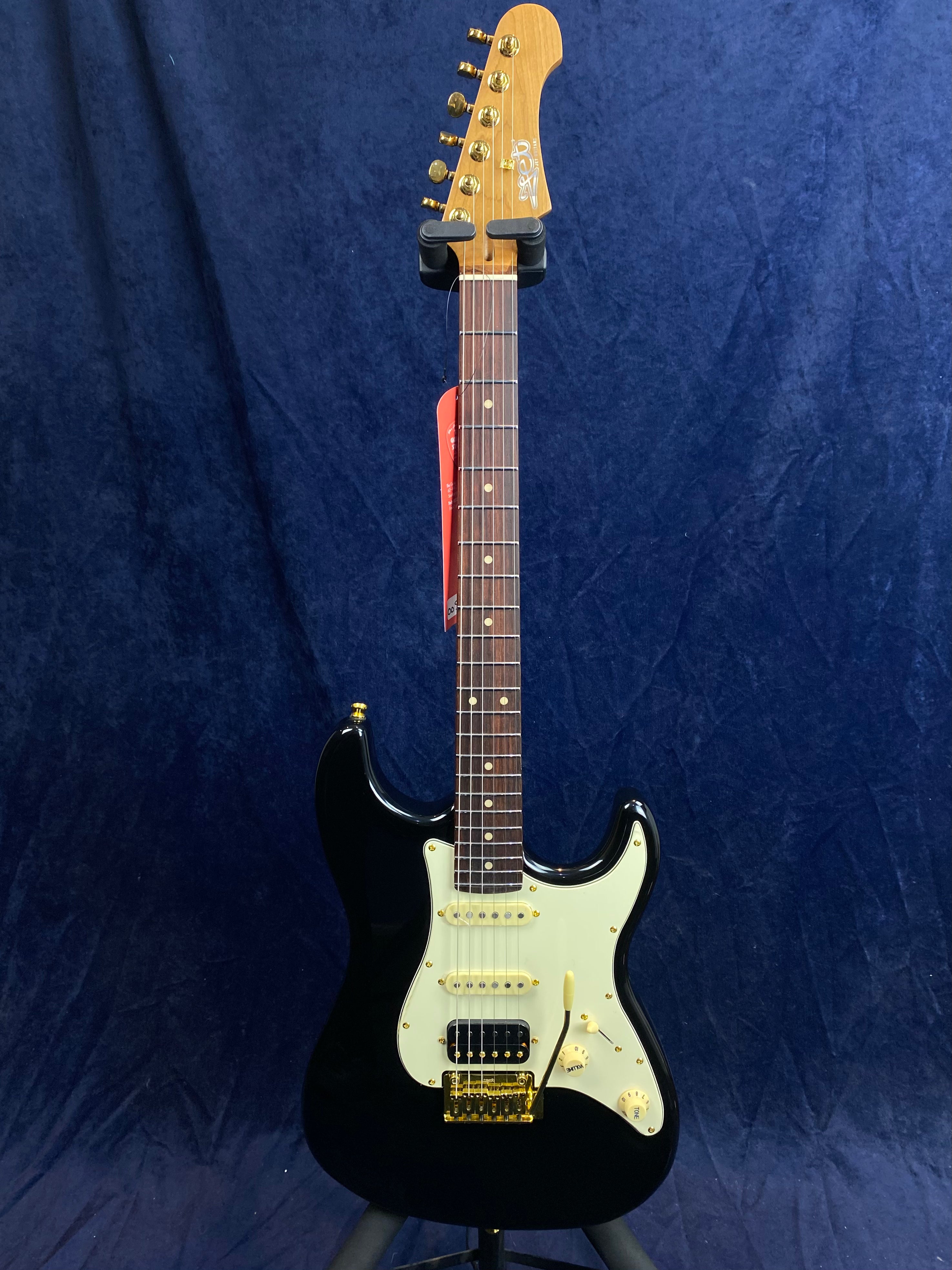 Jet Guitars electric guitar with a black body, cream pickguard, gold hardware, and a maple headstock on a dark blue background.