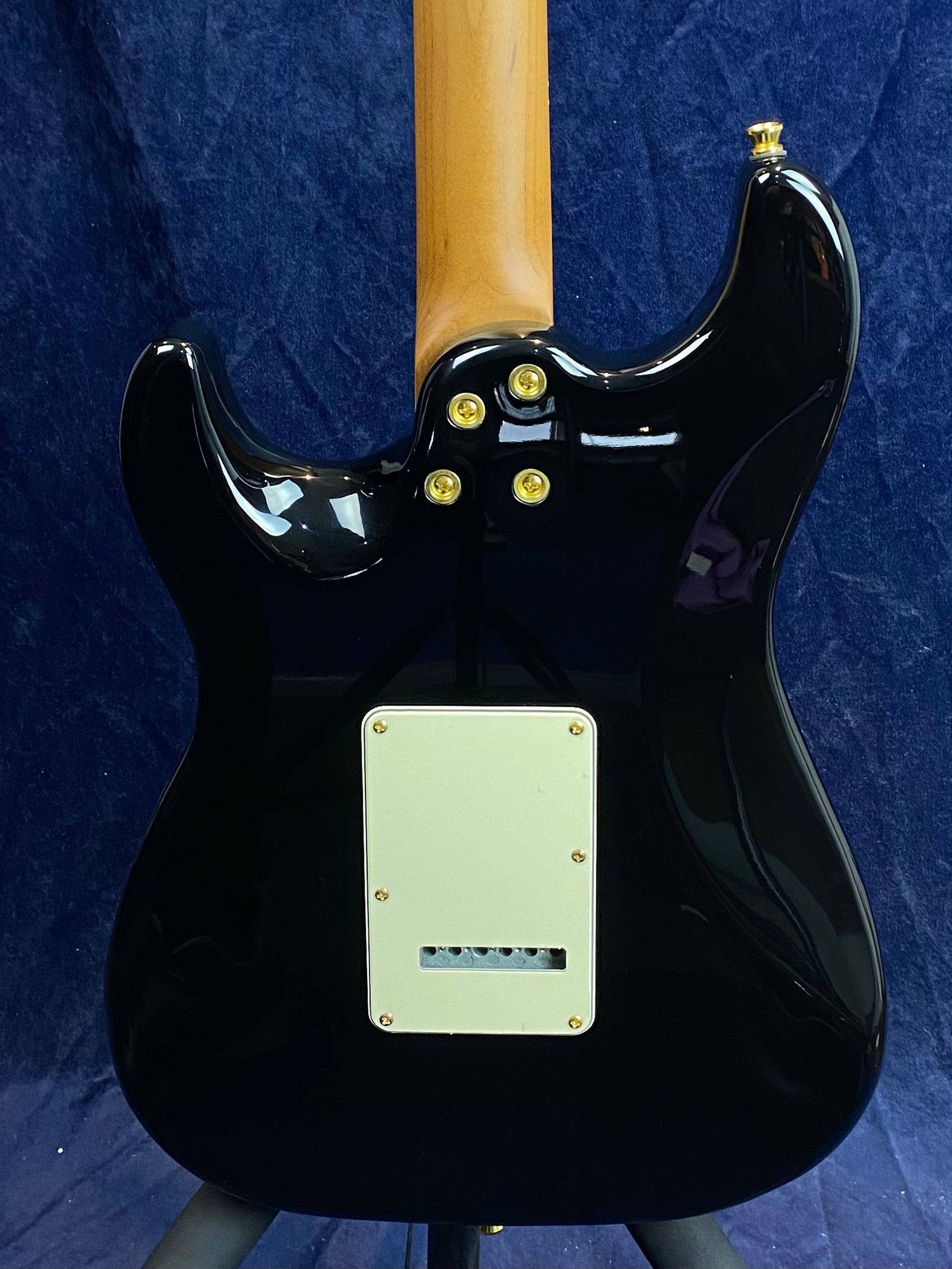 Black Jet Guitar viewed from the back, showing a natural wood neck, gold screws on the body joint, and a cream-colored rectangular backplate.