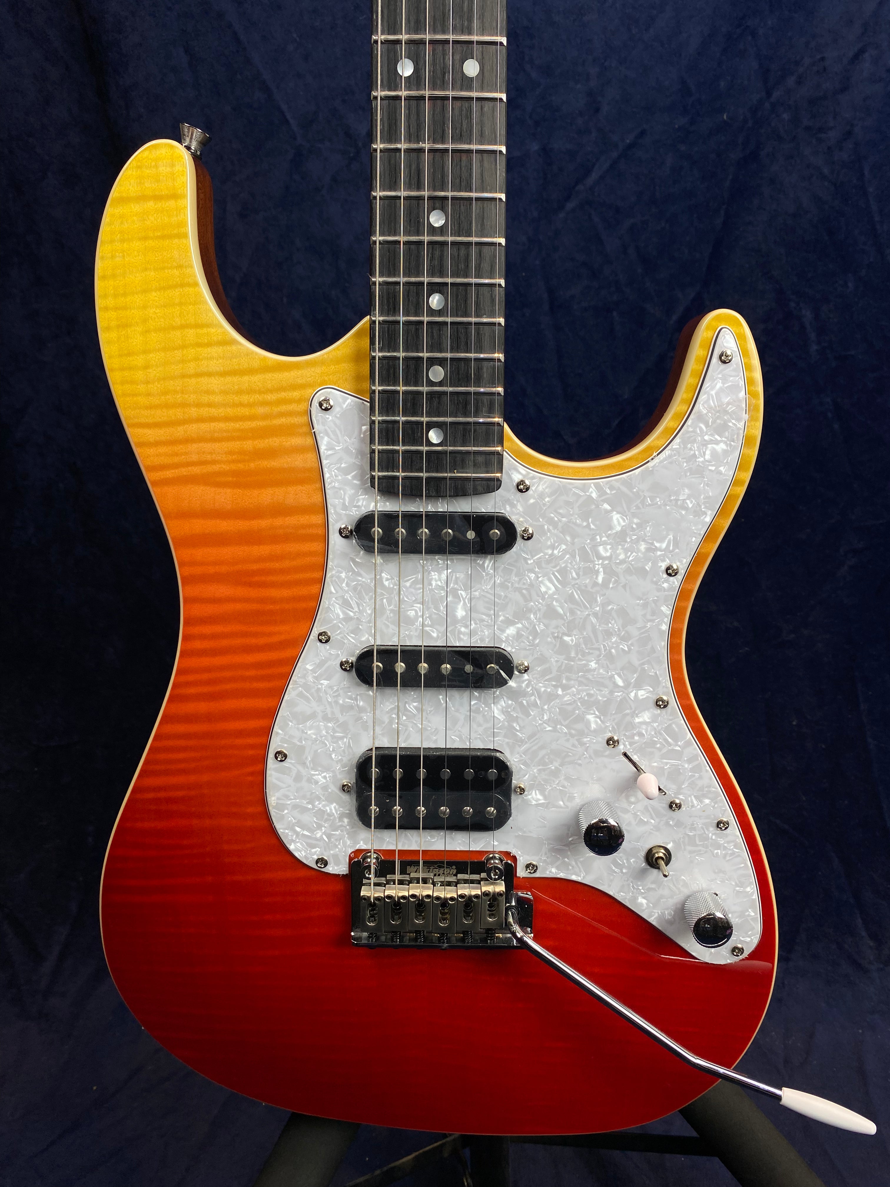 Electric guitar with a red-to-yellow sunburst body, white pearloid pickguard, three pickups, and a whammy bar.