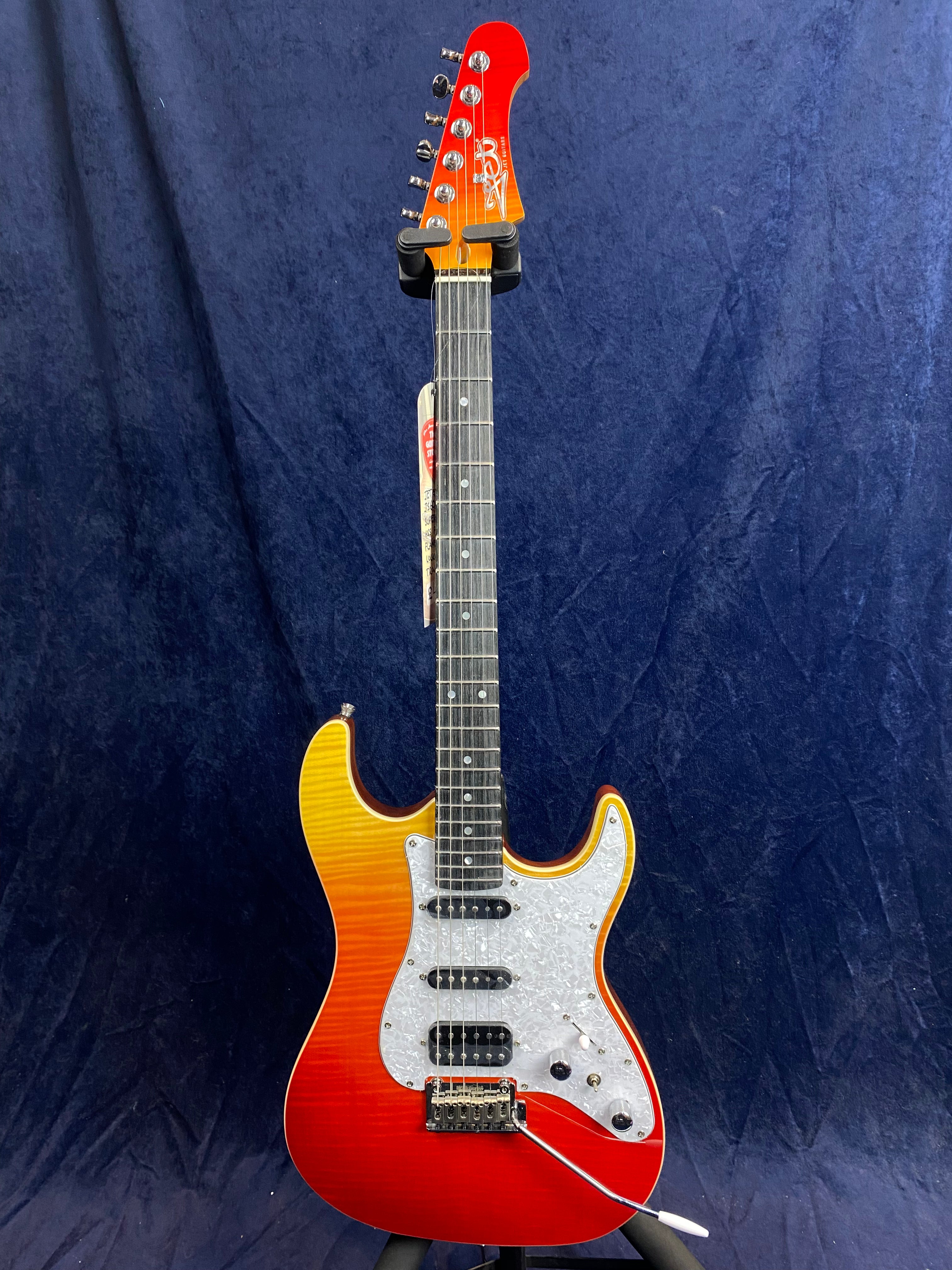 Electric guitar with a sunburst orange to red finish, white pearloid pickguard, three pickups, and a whammy bar, set against a dark blue background.