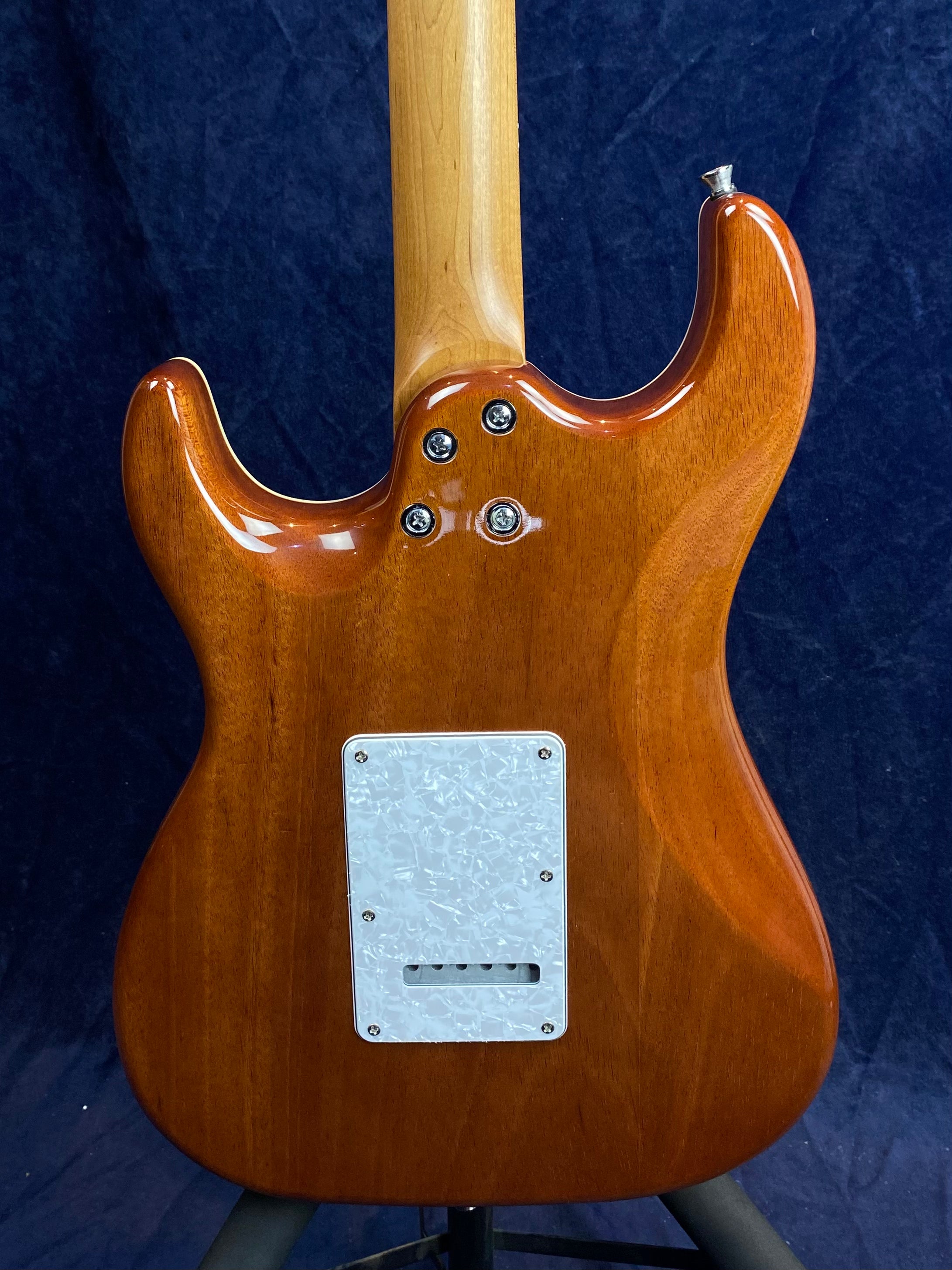 Glossy, brown electric guitar back; light wood neck, four neck bolts, and a white marbled plastic cover plate near the bottom center.