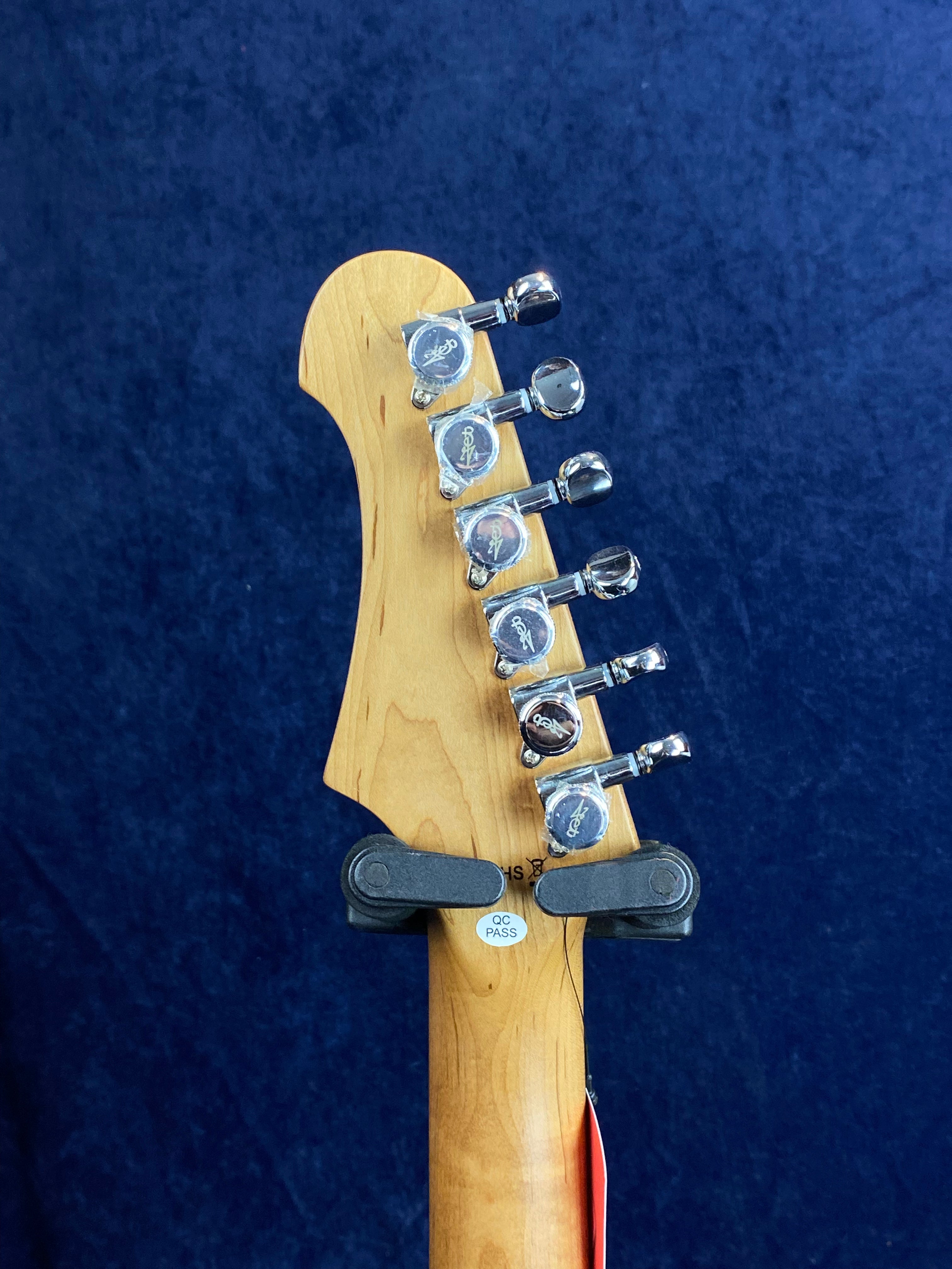 Six chrome tuning pegs line the back of a light wood electric guitar headstock against a dark blue background, with a QC Pass sticker near the base.