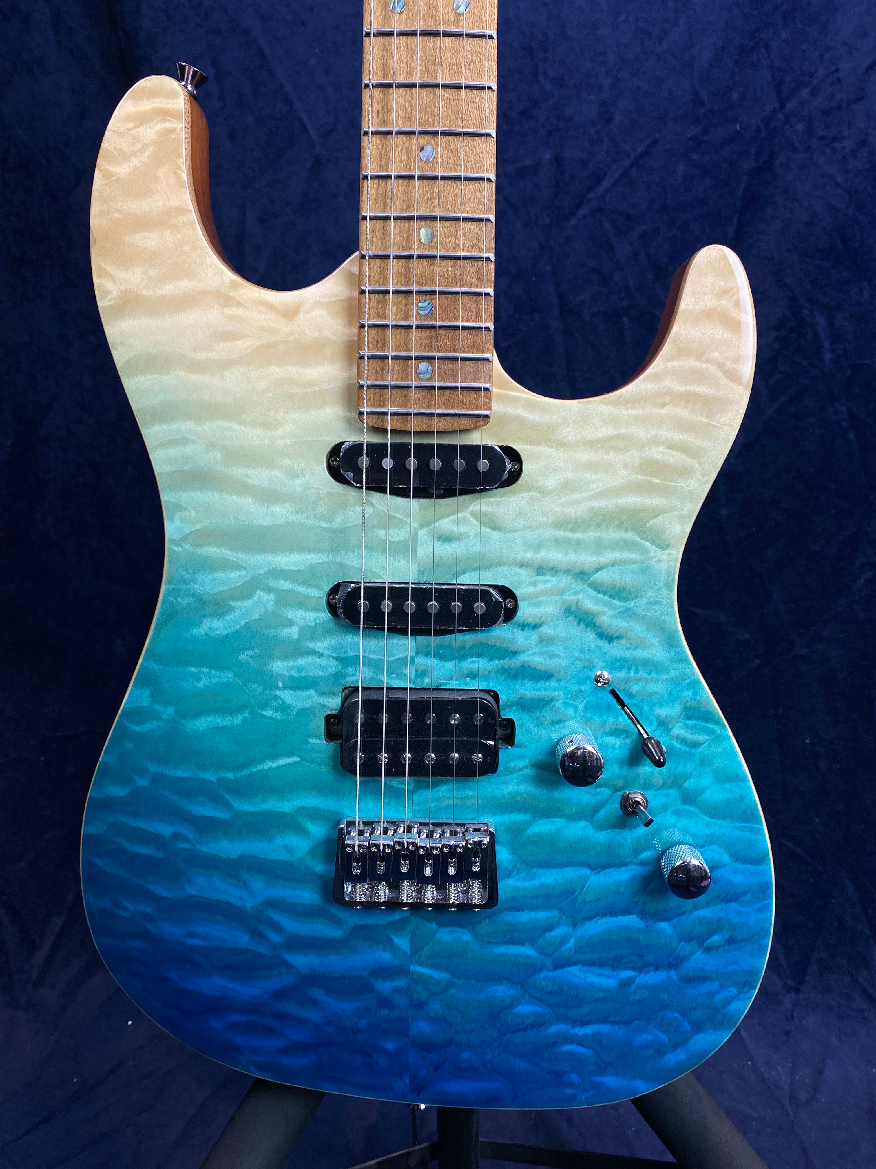 Electric guitar with a quilted maple top, fading from natural wood at the top to turquoise and deep blue at the base, chrome hardware, and three pickups.
