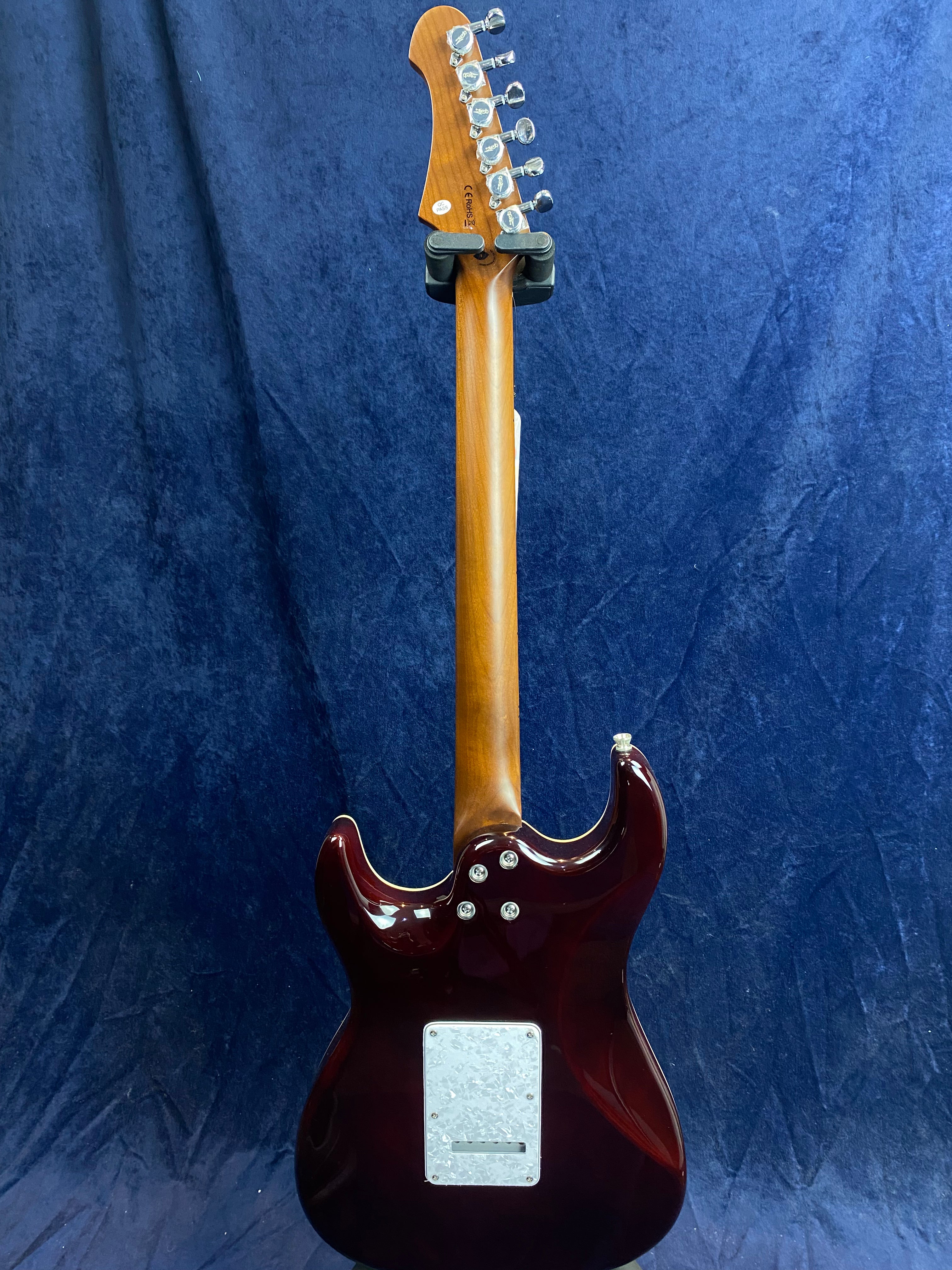 Electric guitar viewed from the back, showing a glossy dark red body, a light brown neck, and silver tuning pegs against a blue background.
