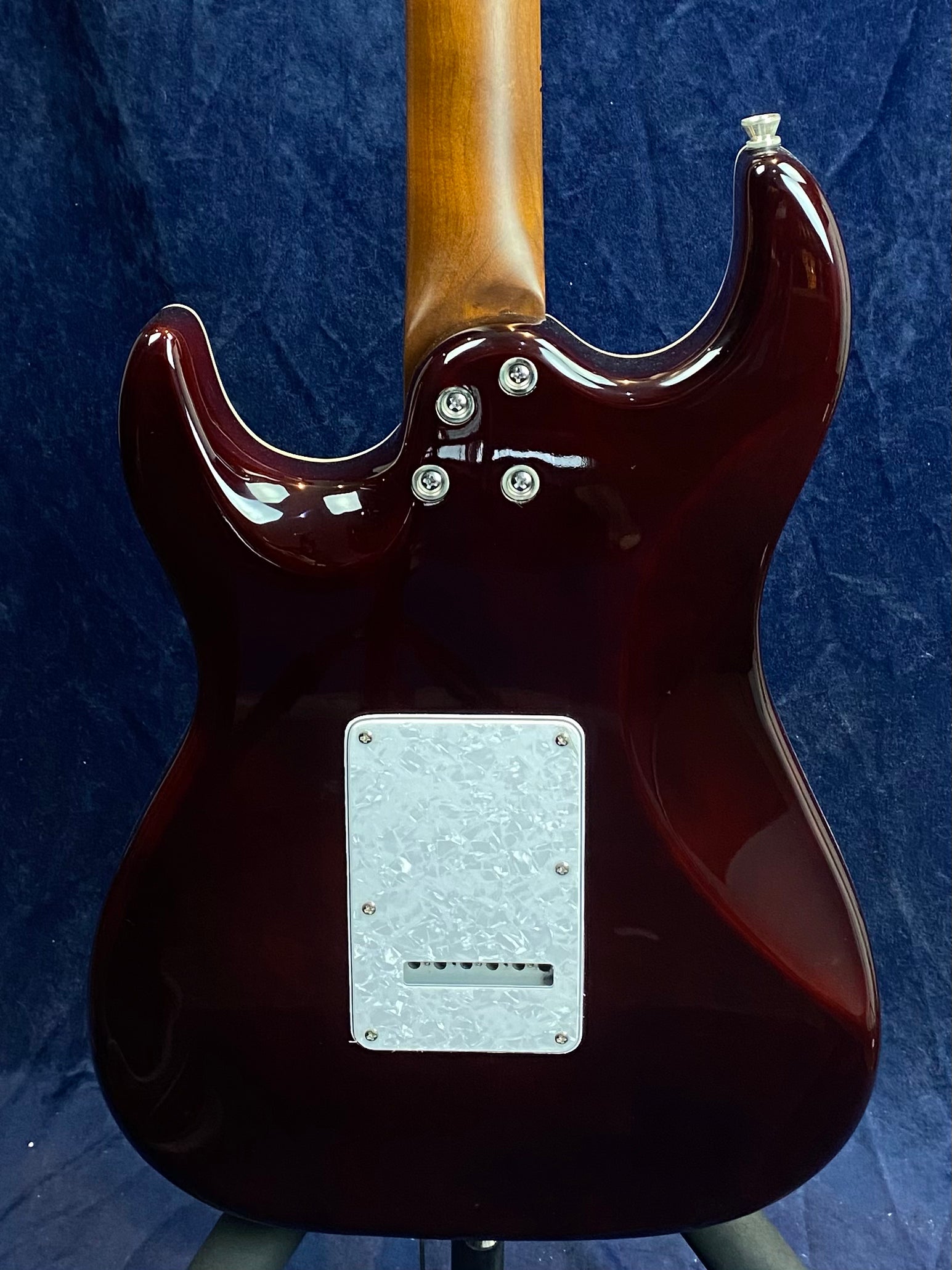 The back of a dark red electric guitar with a brown neck, silver neck bolts, and a rectangular white cover plate near the bottom.
