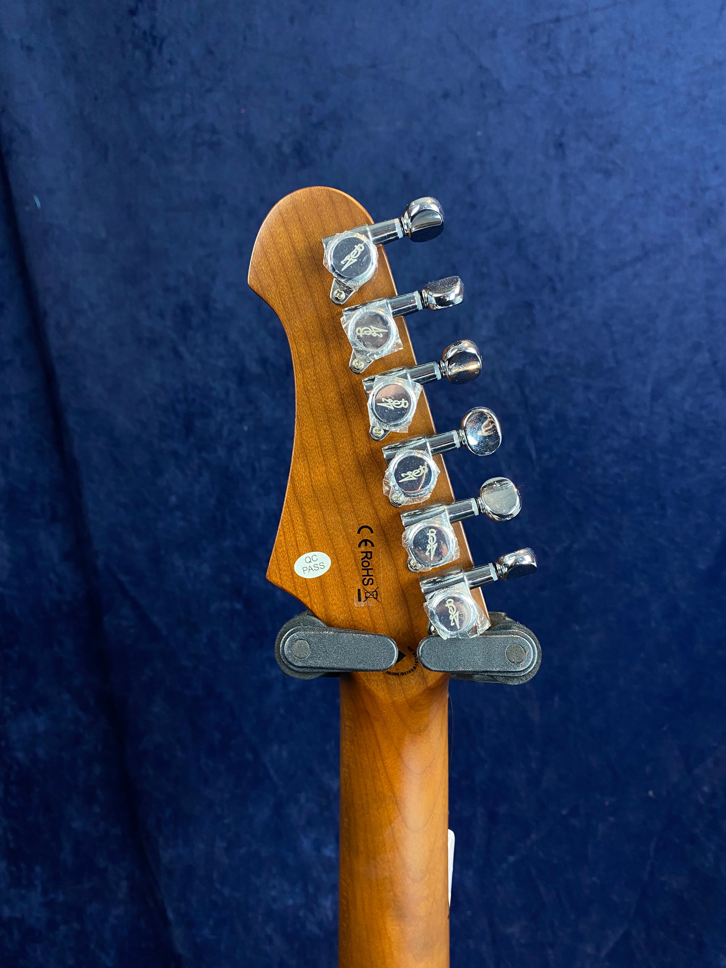 Six chrome tuning pegs on the headstock of a wooden electric guitar neck, with visible certification stickers and a dark blue background.