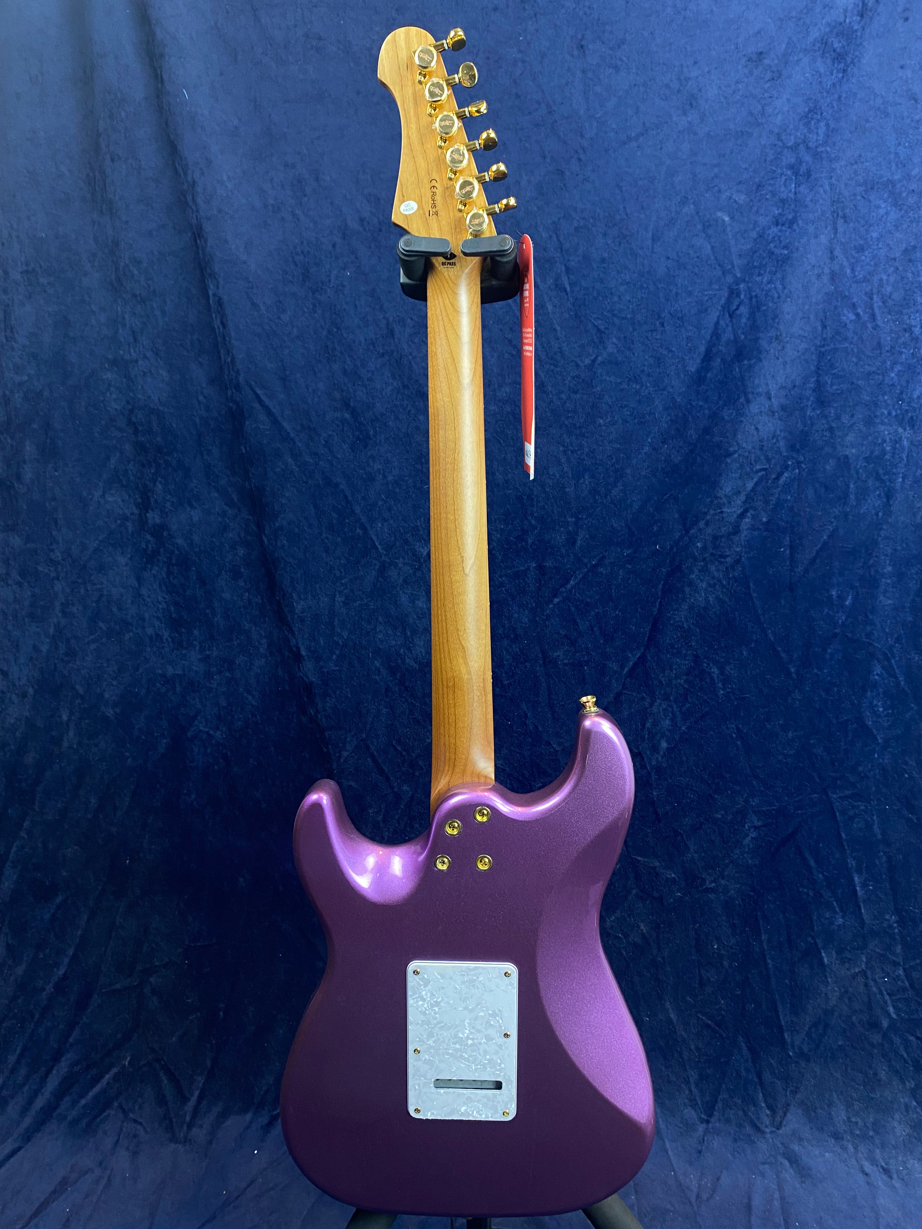 Purple electric guitar shown from the back with a natural wood neck, gold tuning pegs, and a white electronics cover plate near the bottom.