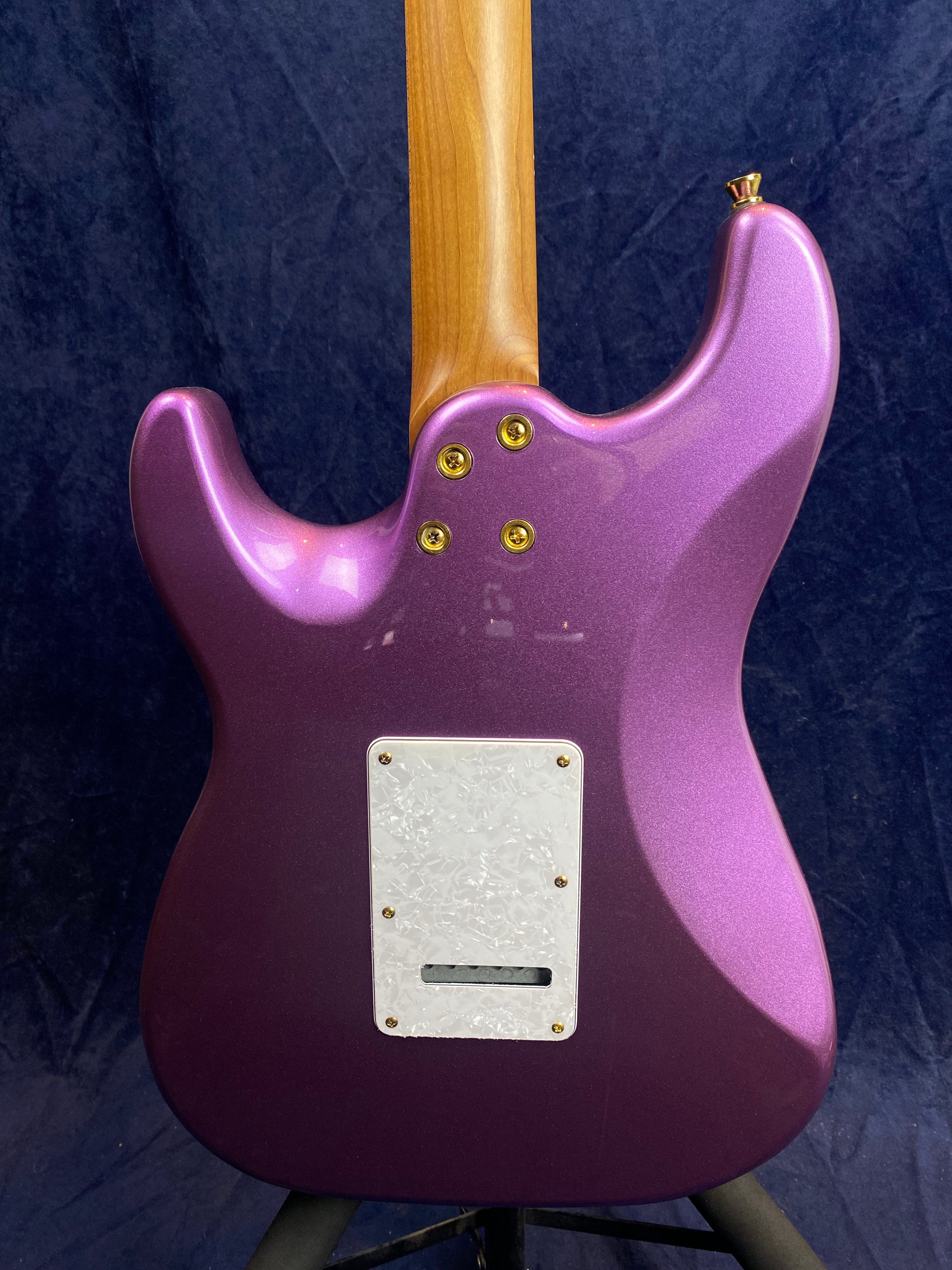 Metallic purple electric guitar back, maple neck, white pearloid backplate with gold screws, four bolt neck joint, dark blue background.