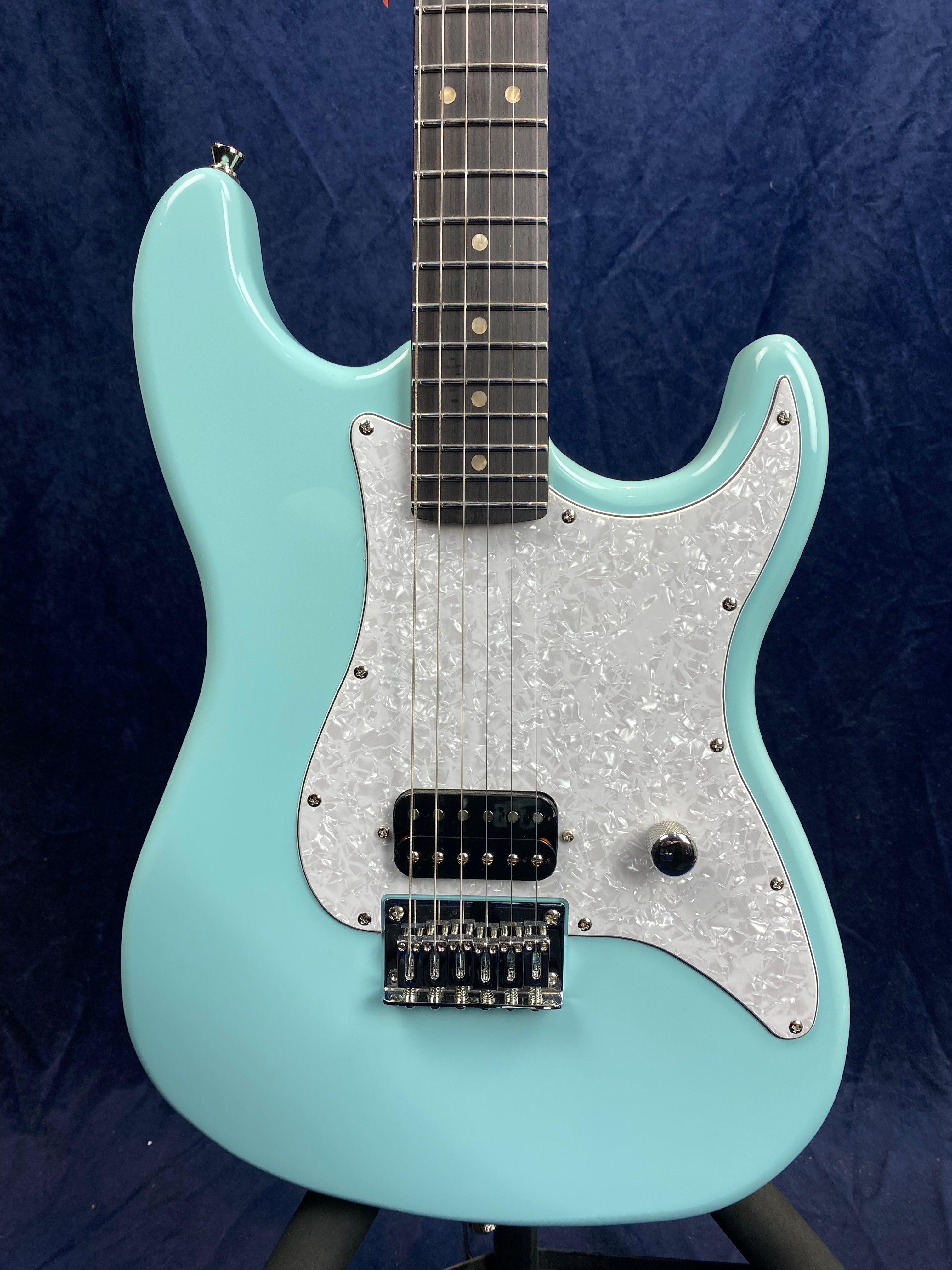 Light blue electric guitar with a white pearloid pickguard, single humbucker pickup, one control knob, six strings, and a dark wood fretboard.