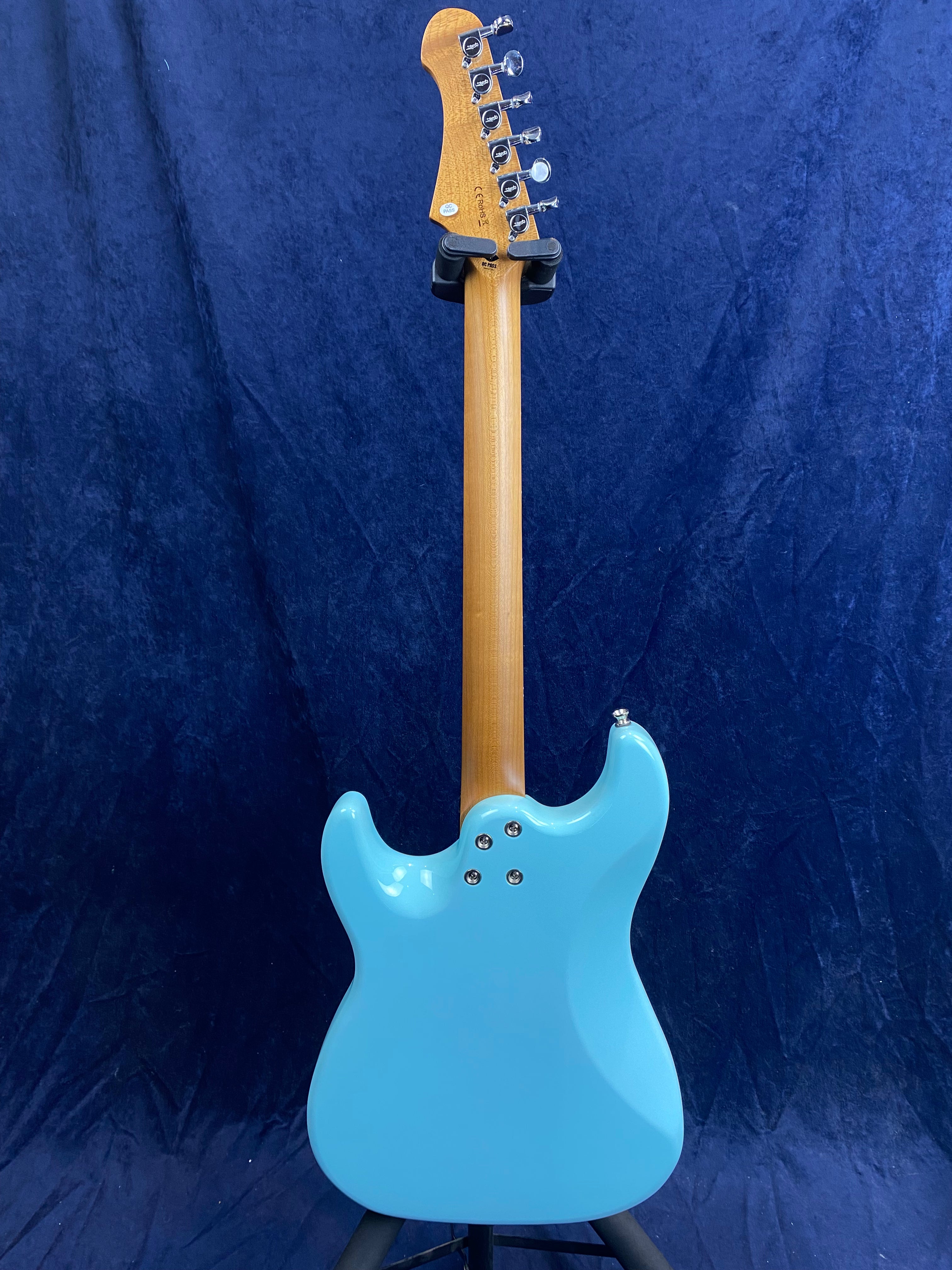 A light blue electric guitar viewed from the back, showing a wooden neck, six tuning pegs, and a contoured body against a dark blue background.
