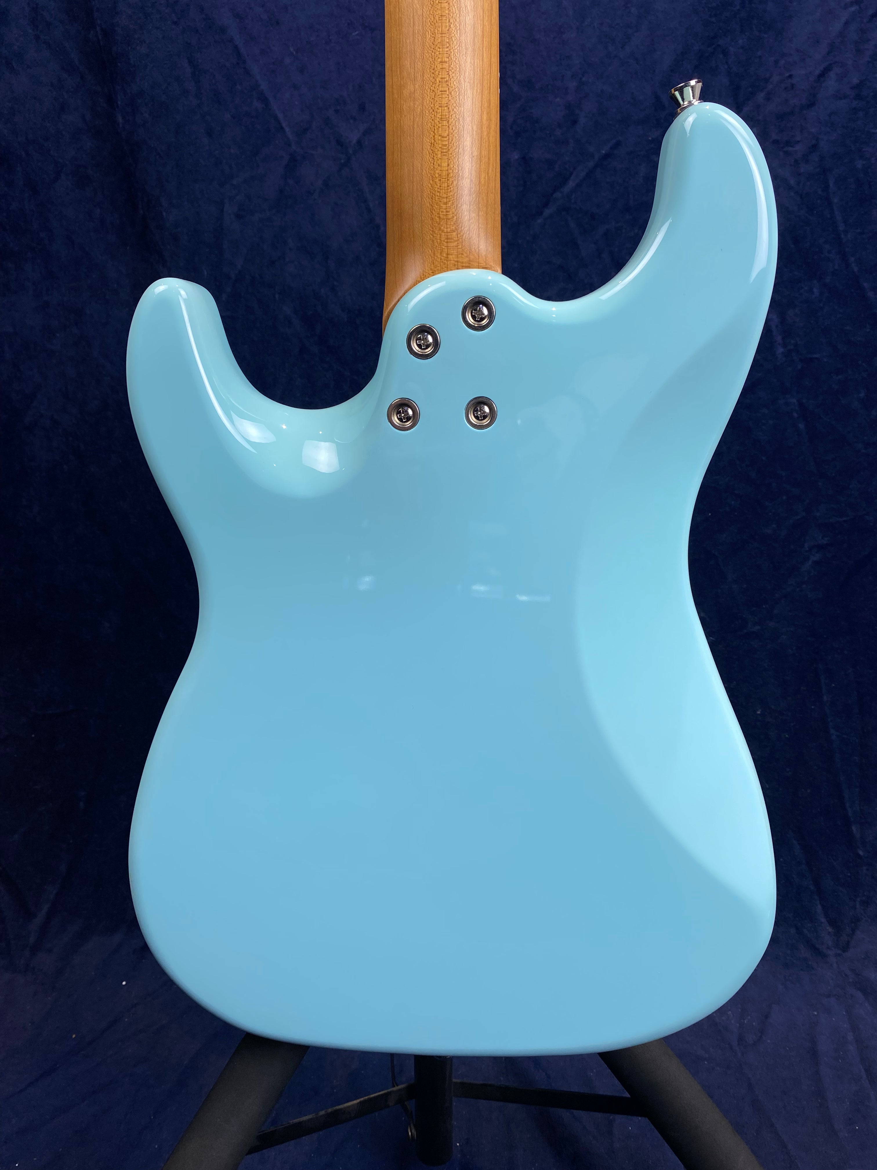 Light blue electric guitar back with a natural wood neck, four metal neck screws, and curved body contours against a dark background.