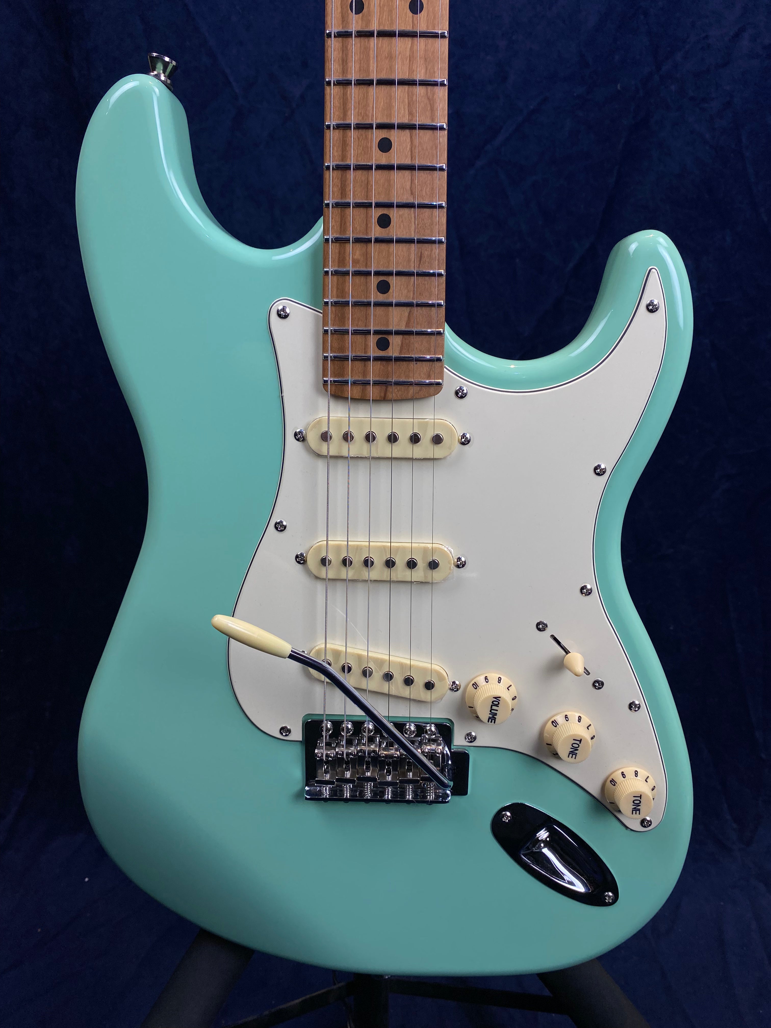 Aqua blue electric guitar with white pickguard, three cream single-coil pickups, three control knobs, and a chrome tremolo bridge.