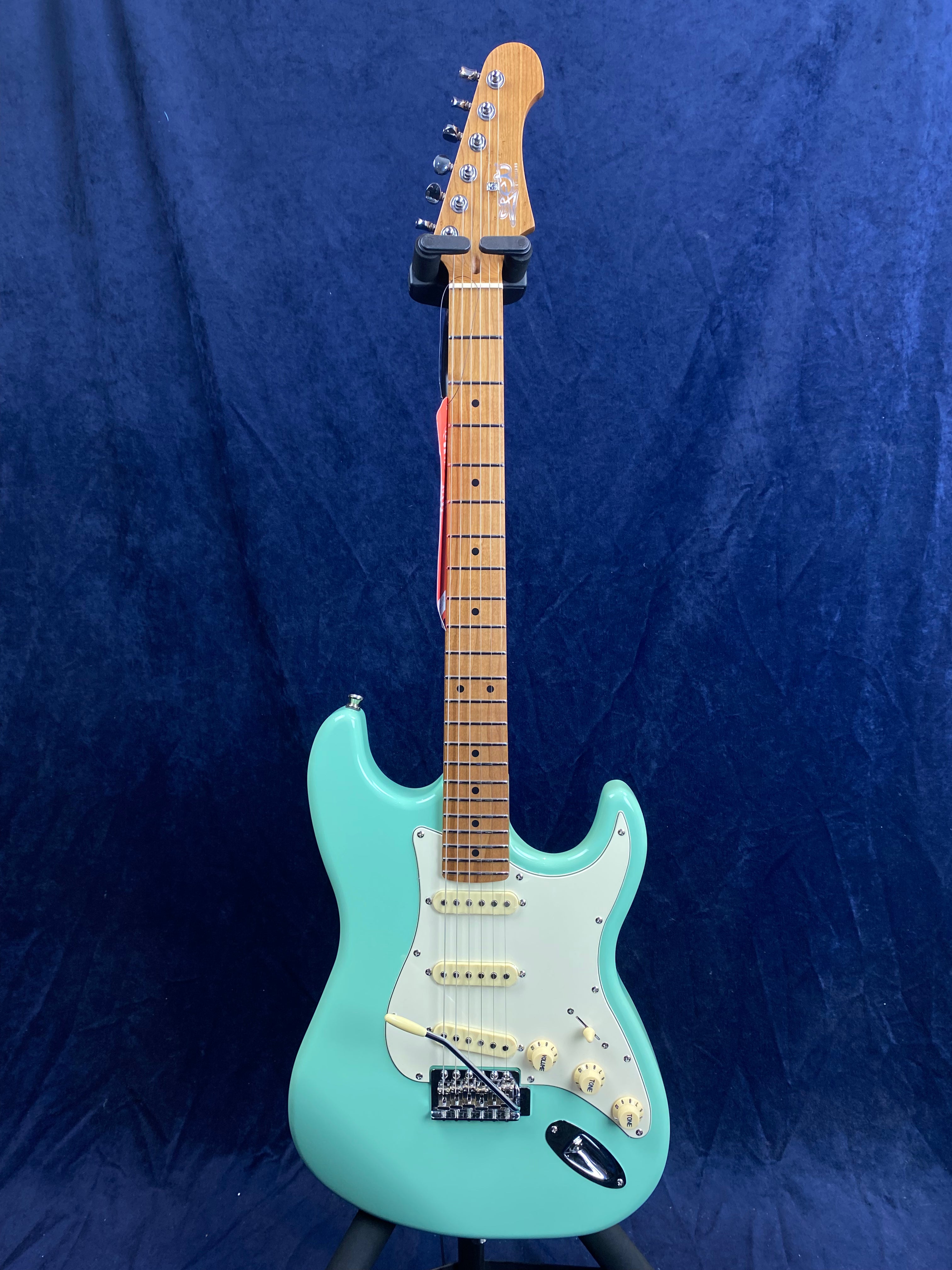 Seafoam green electric guitar with a white pickguard, three single-coil pickups, and a light-colored maple neck and fretboard.
