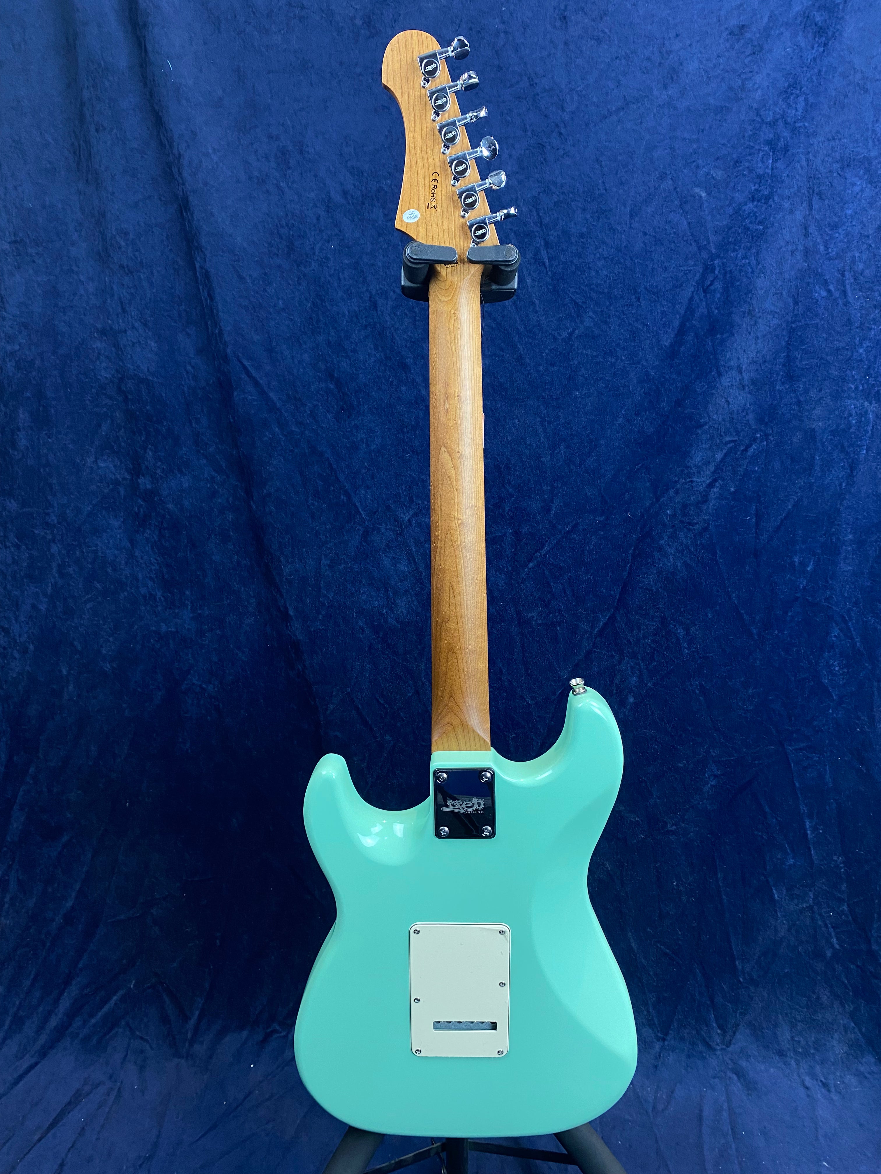 Aqua blue electric guitar shown from the back, with a natural wood neck, six tuning pegs, and white rectangular backplate.