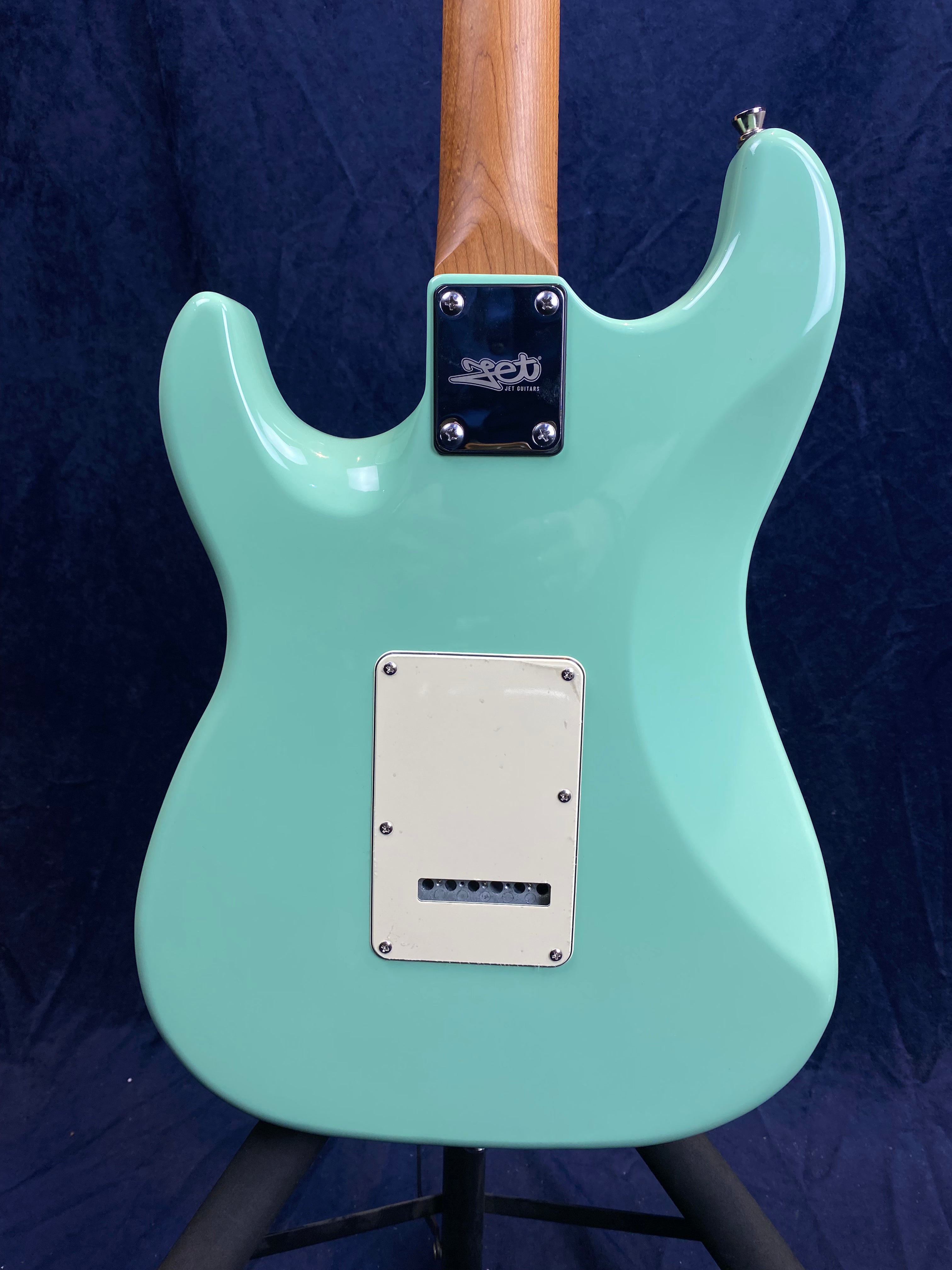 Light turquoise electric guitar body with a white plastic plate on the back and a wooden neck attached by a metal plate with four screws.