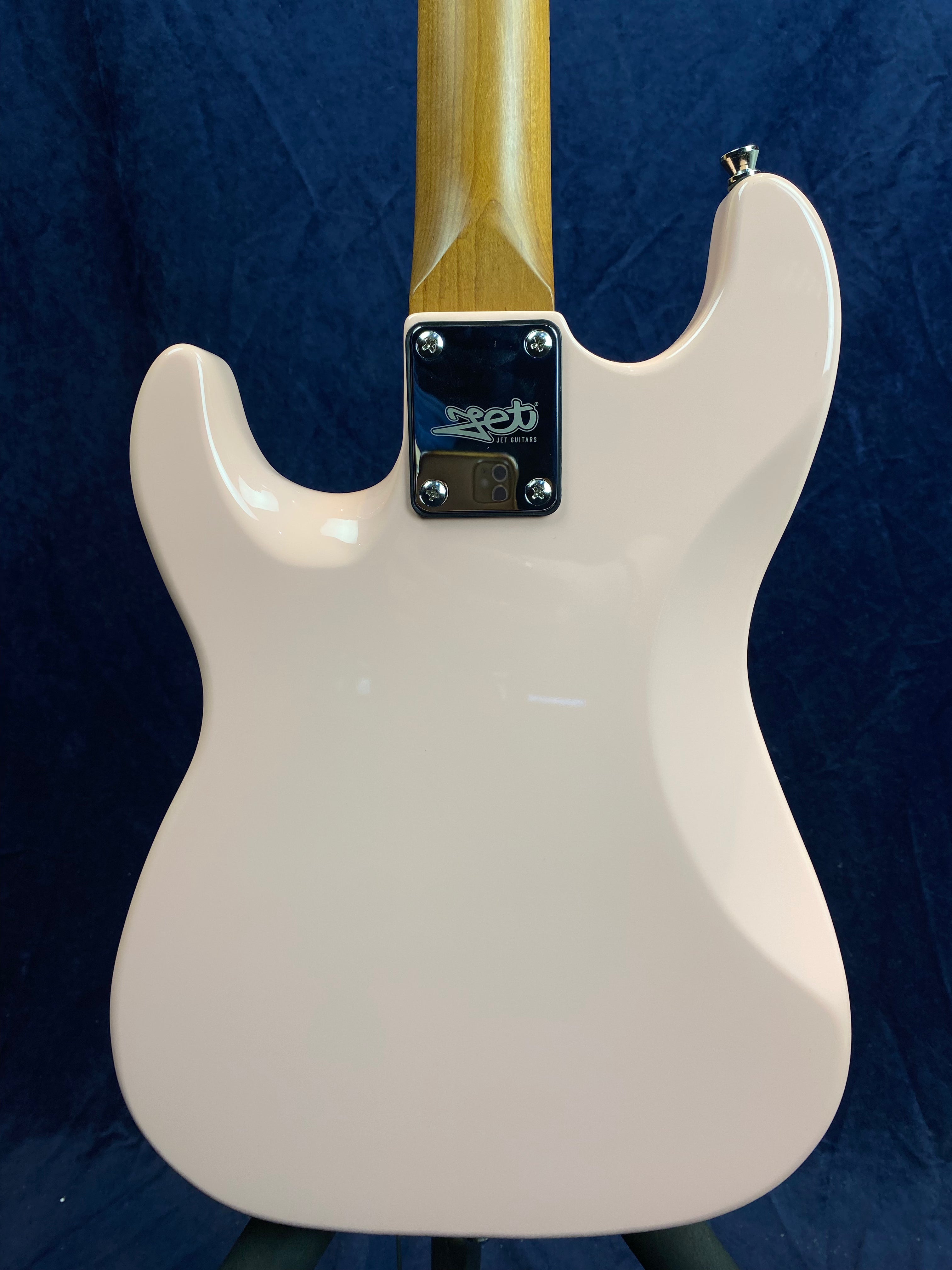 Rear view of a light pink electric guitar body with a natural wood neck and a silver neck plate engraved with the Jet Guitars logo.