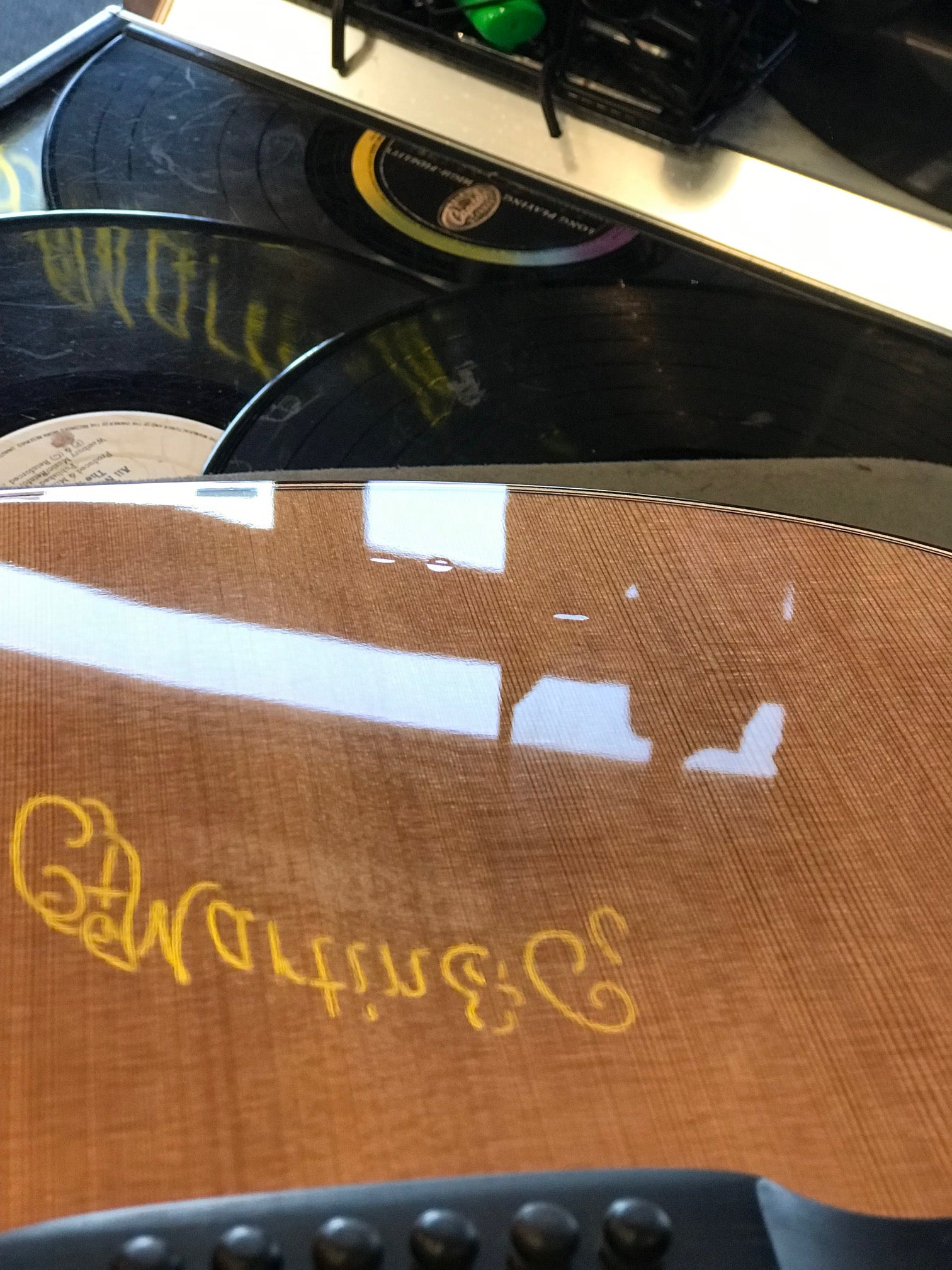 Wooden acoustic guitar body reflecting vinyl records and white ceiling lights, with the yellow Martin & Co. logo visible on the guitar's surface.