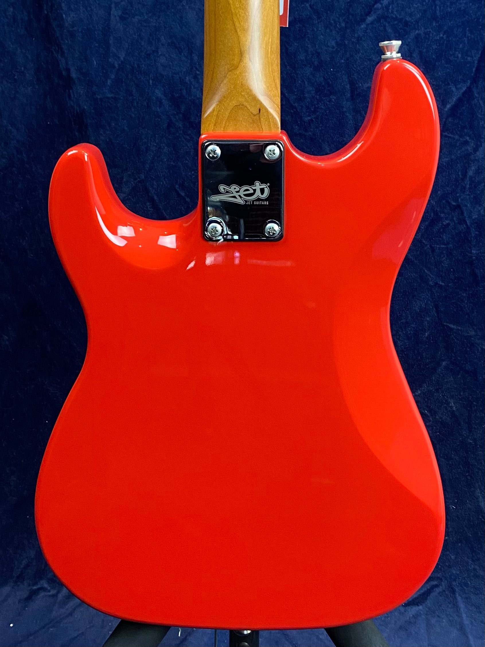 Bright red electric guitar body with a natural wood neck and a metal neck plate engraved with the Jet Guitars logo.