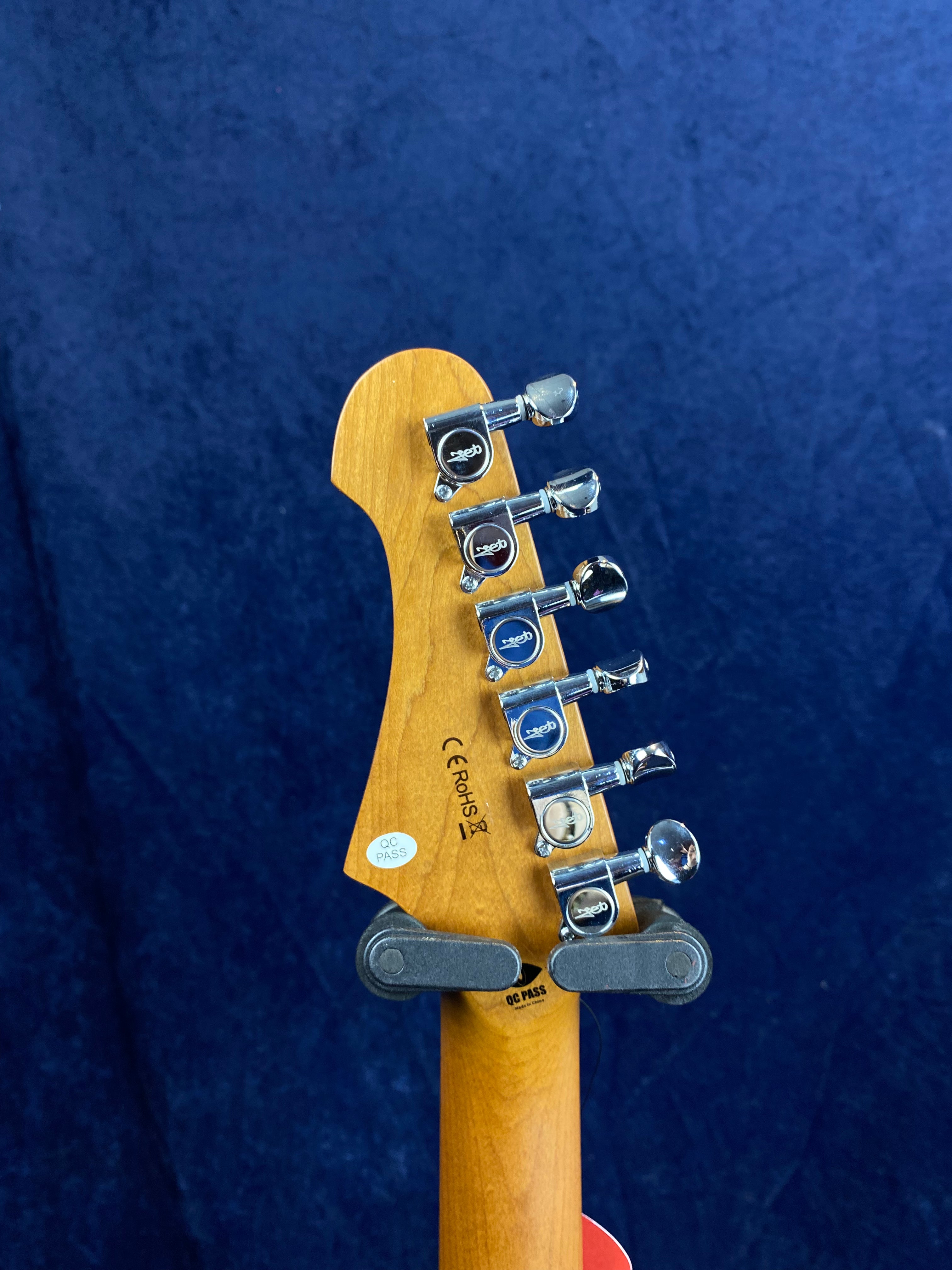 Six chrome tuning pegs on a Jet Guitars headstock with visible QC PASS and CE ROHS stickers, against a dark blue background.