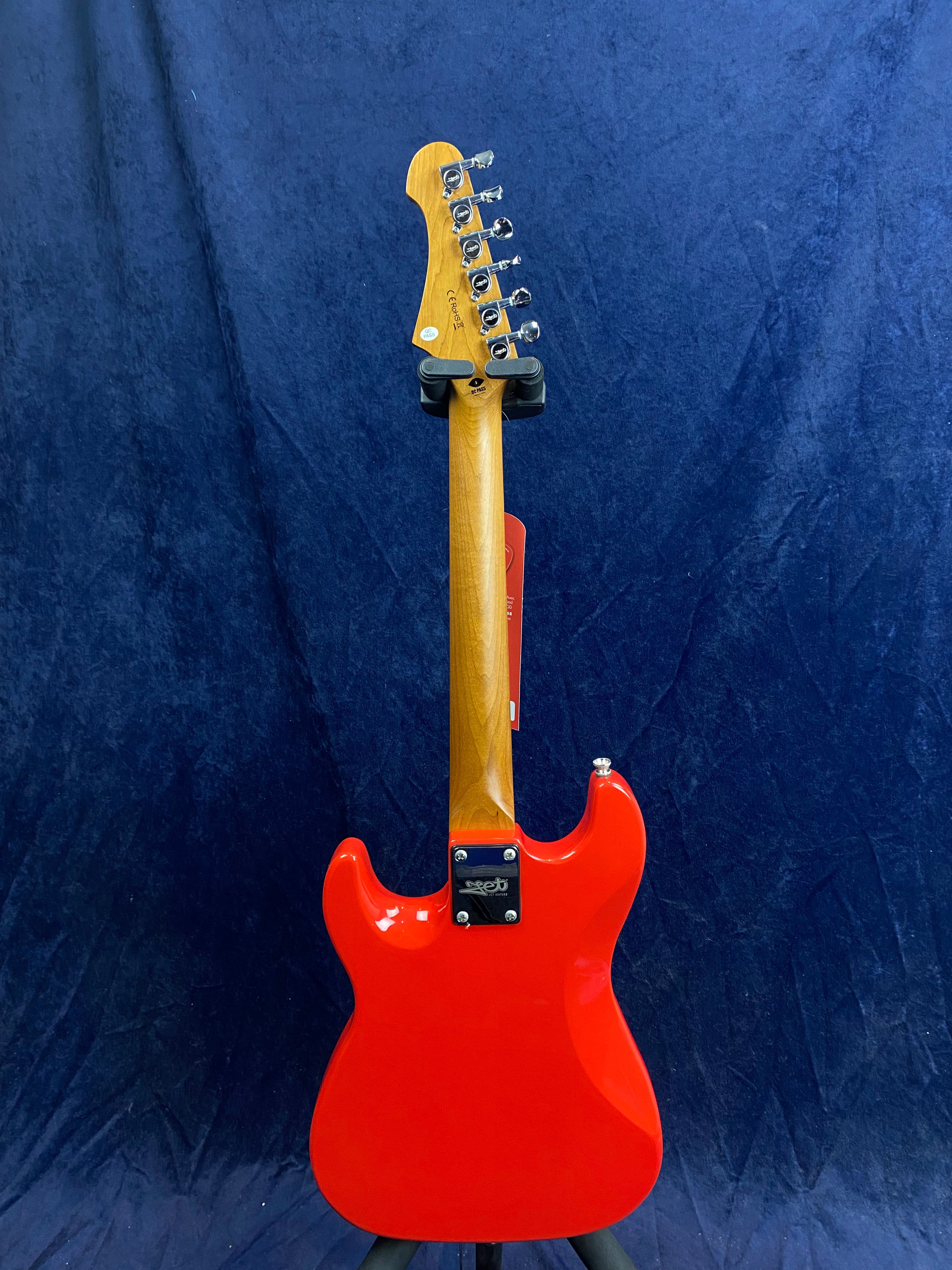 Bright red electric Jet Guitar shown from the back, with a natural wood neck and chrome tuners against a dark blue textured background.