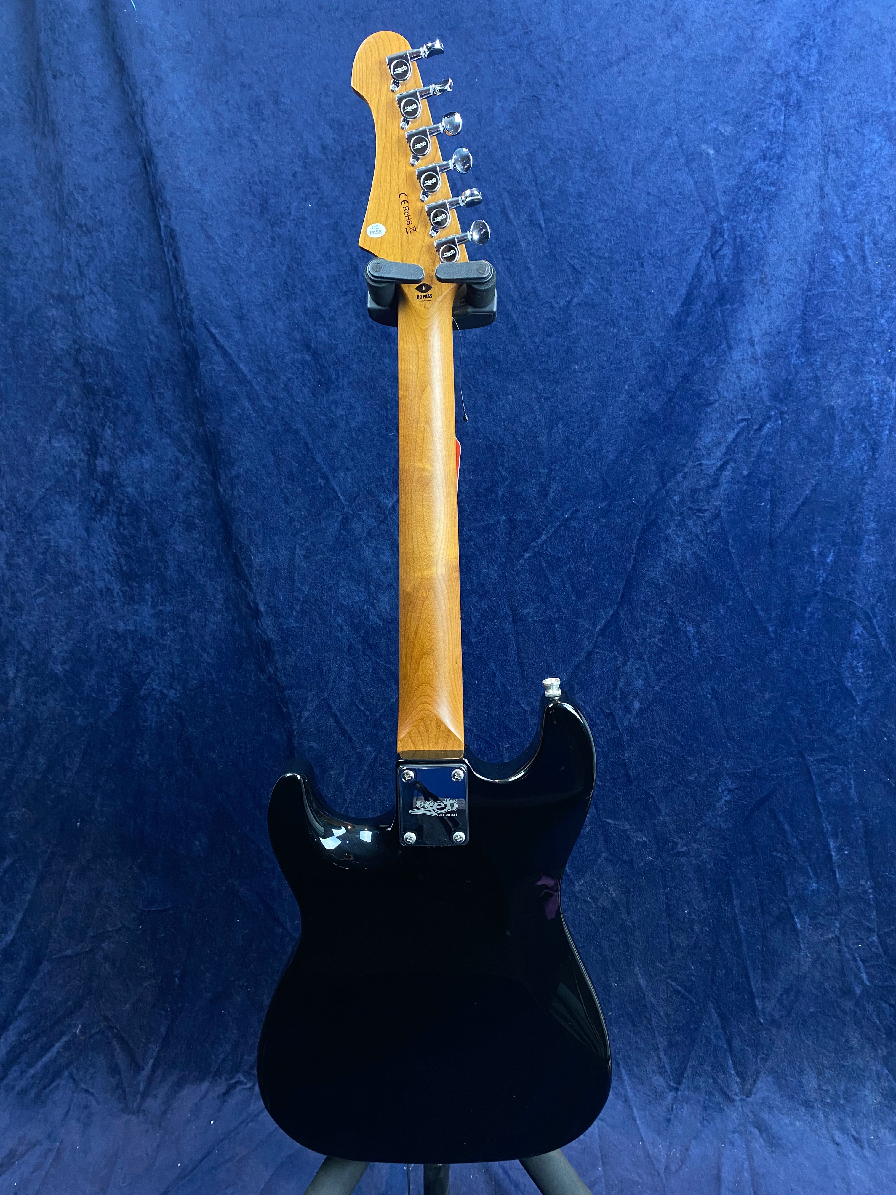 Electric guitar shown from the back: glossy black body, natural wood neck, chrome tuning pegs, set against a blue textured background.