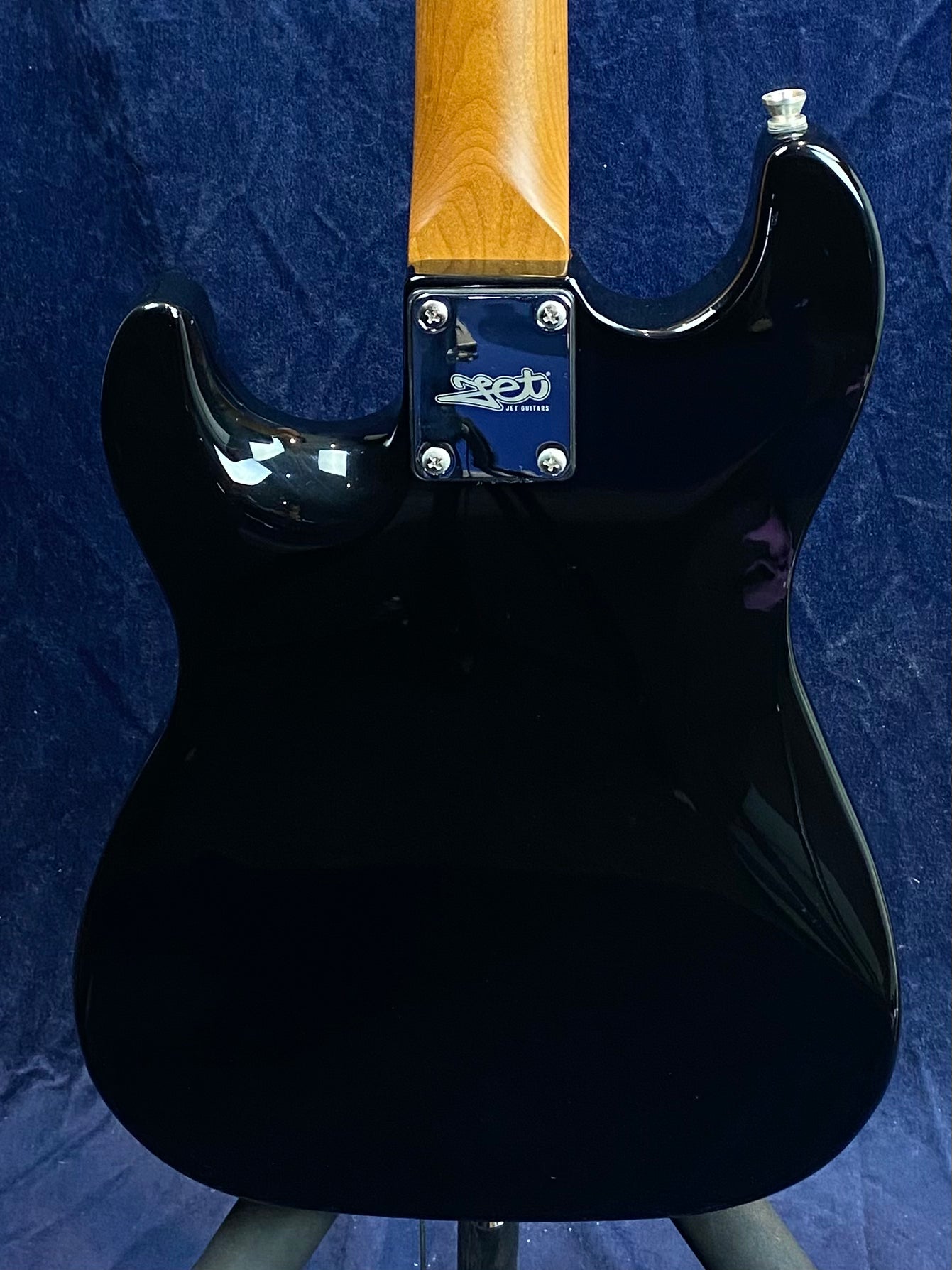 Back view of a black electric guitar body with a natural wood neck and a metal plate reading "Jet Guitars" at the neck joint.