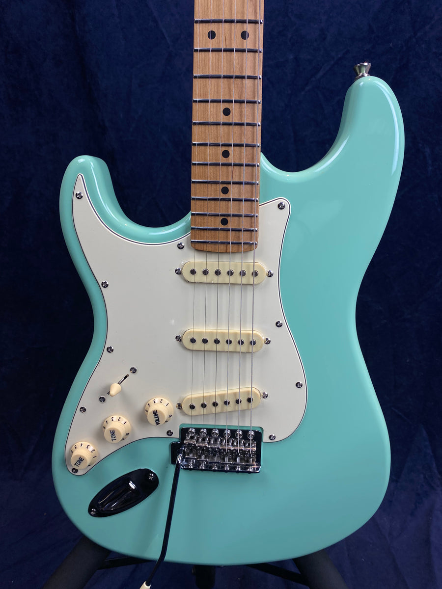 A seafoam green electric guitar with three cream pickups, white pickguard, and light wood neck and fretboard. Knobs for tone and volume are cream colored.