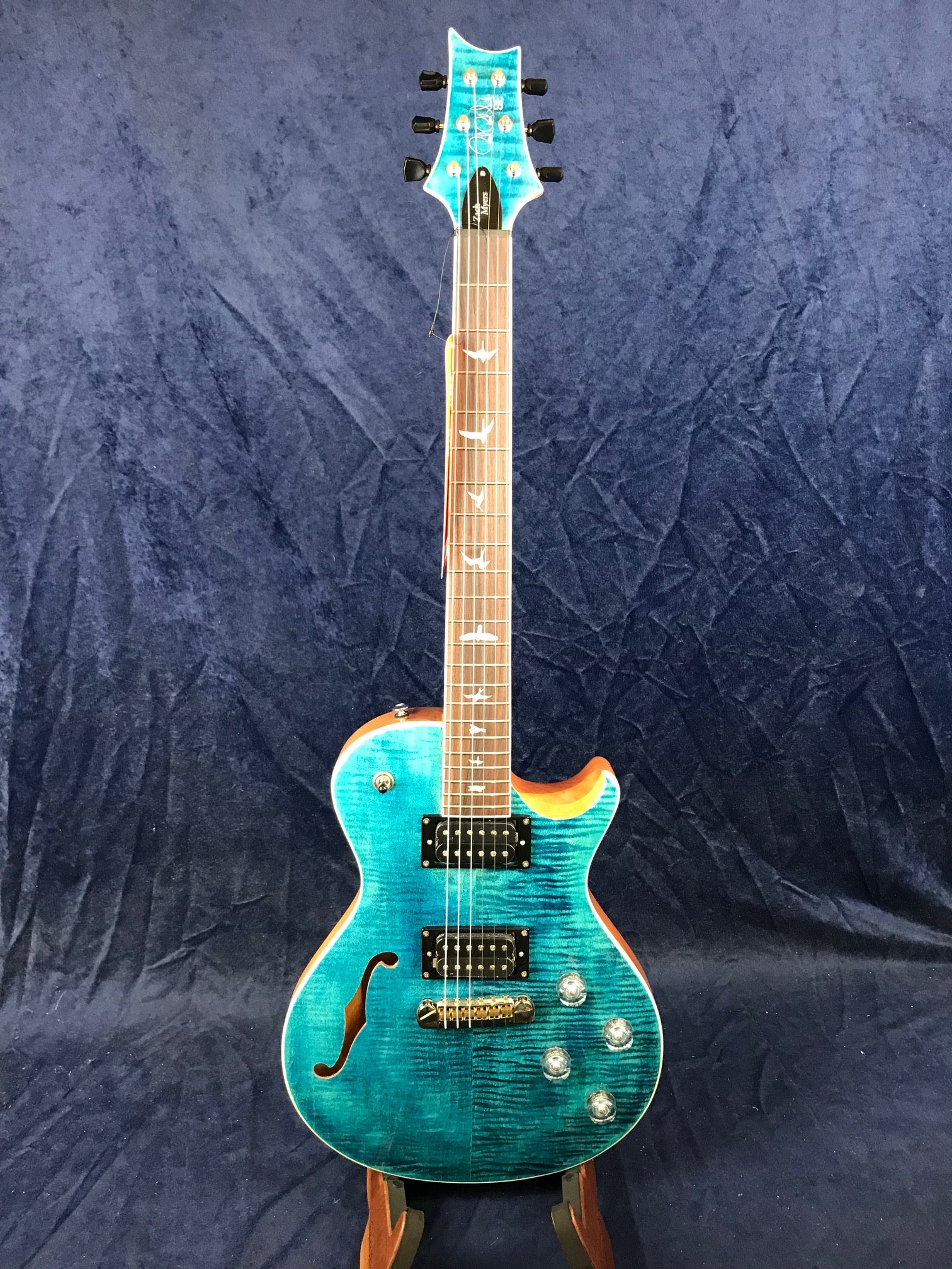 A blue electric guitar with a single cutaway, two humbucker pickups, F-hole, four control knobs, and bird-shaped inlays on the fretboard.