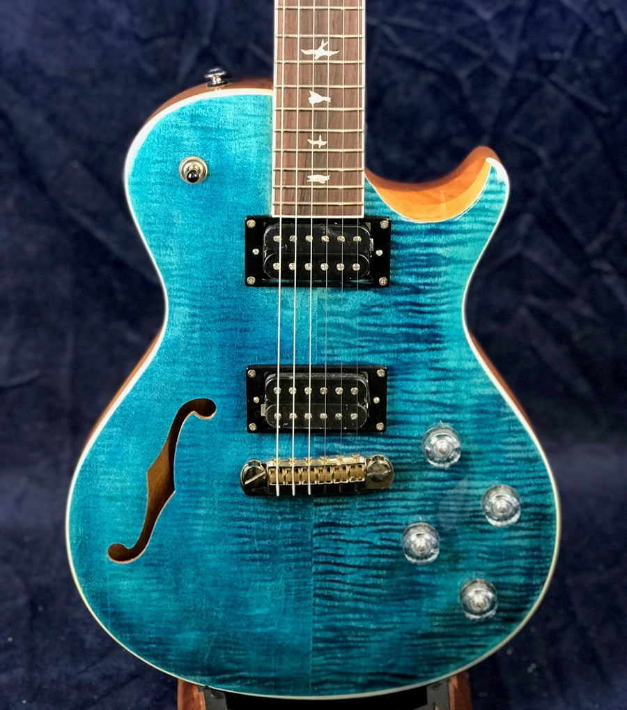 Blue electric guitar with a glossy finish, two humbucker pickups, four control knobs, and a single f-hole on the left side of the body.