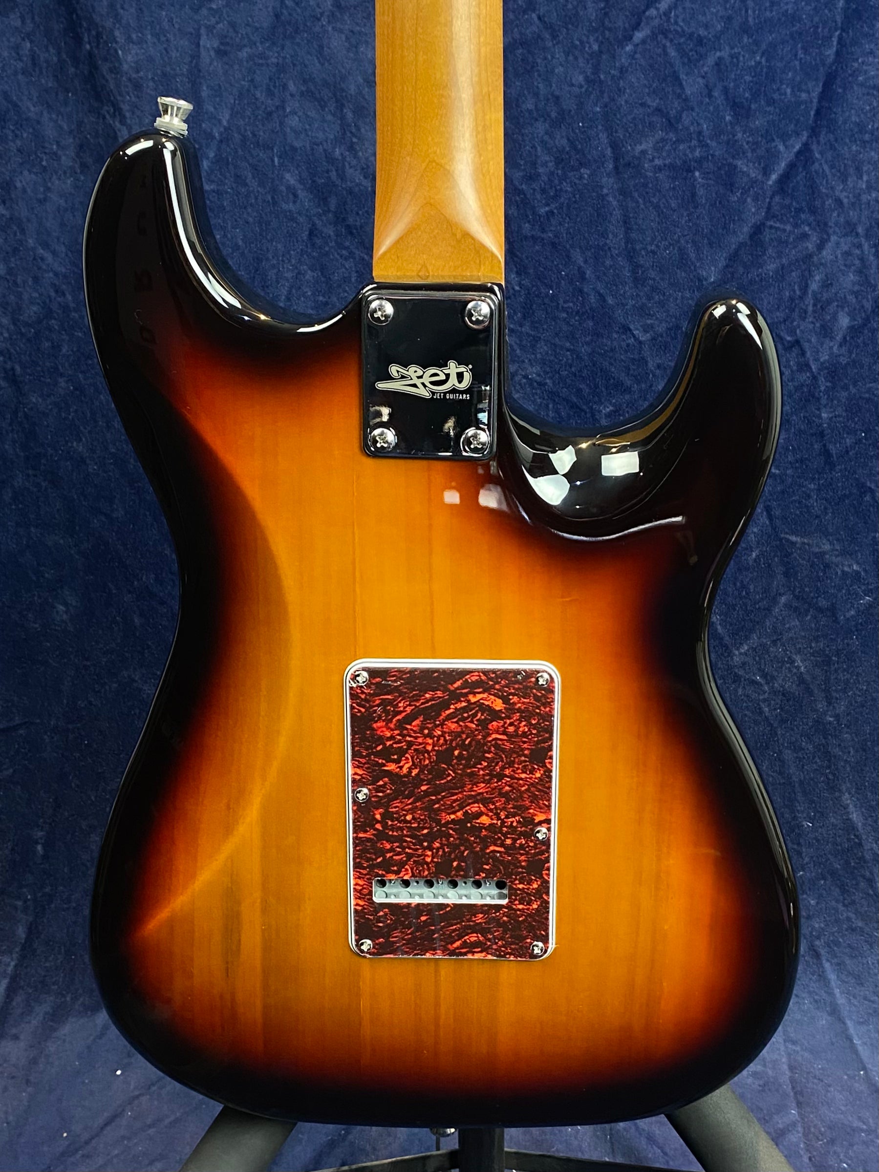 Sunburst electric guitar back with a red tortoiseshell cover plate, bolt-on neck, and chrome neck plate that has a logo and four screws.