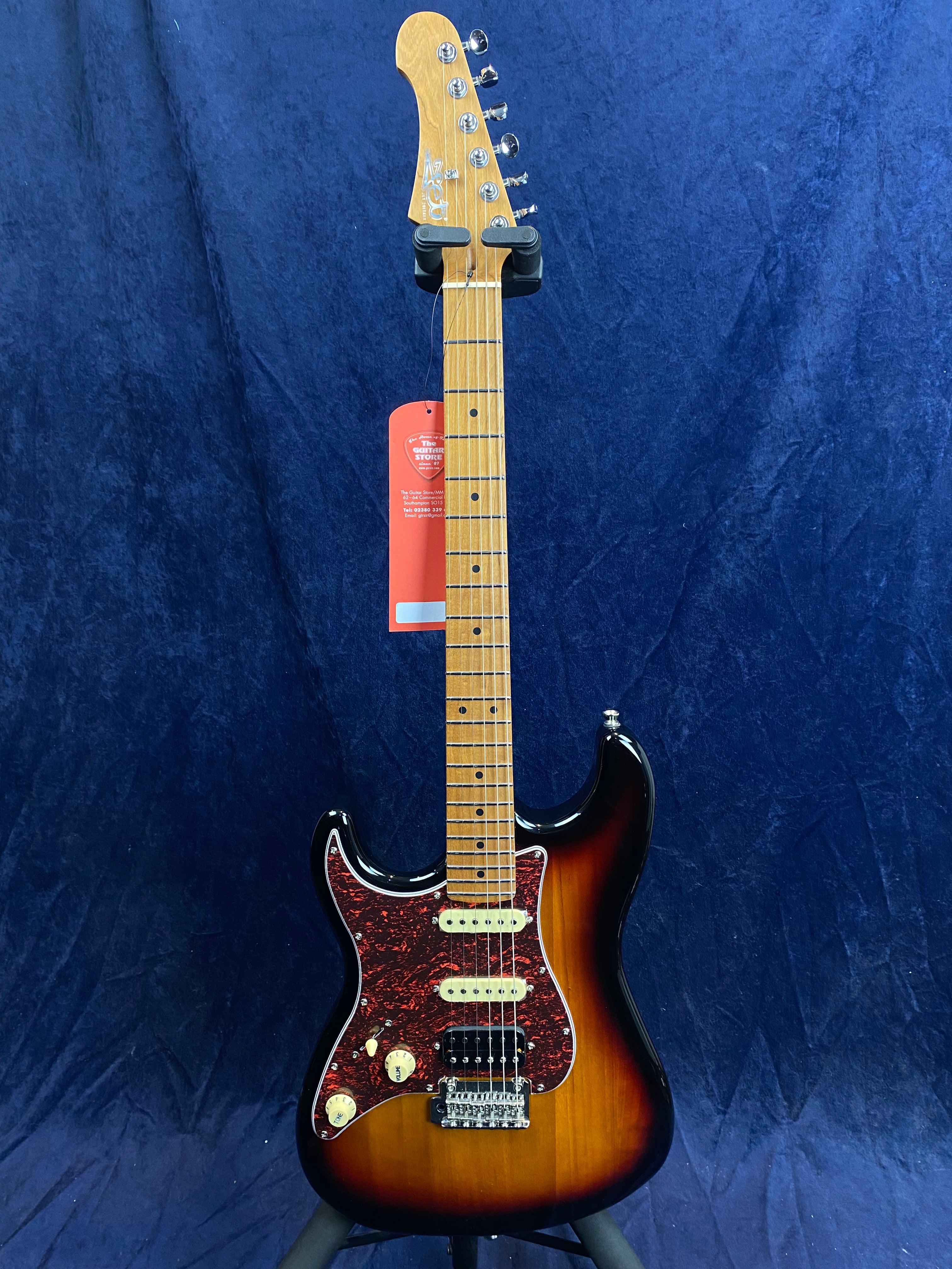 Electric guitar with a sunburst finish, maple neck, three pickups, tortoiseshell pickguard, and cream control knobs against a dark blue background.