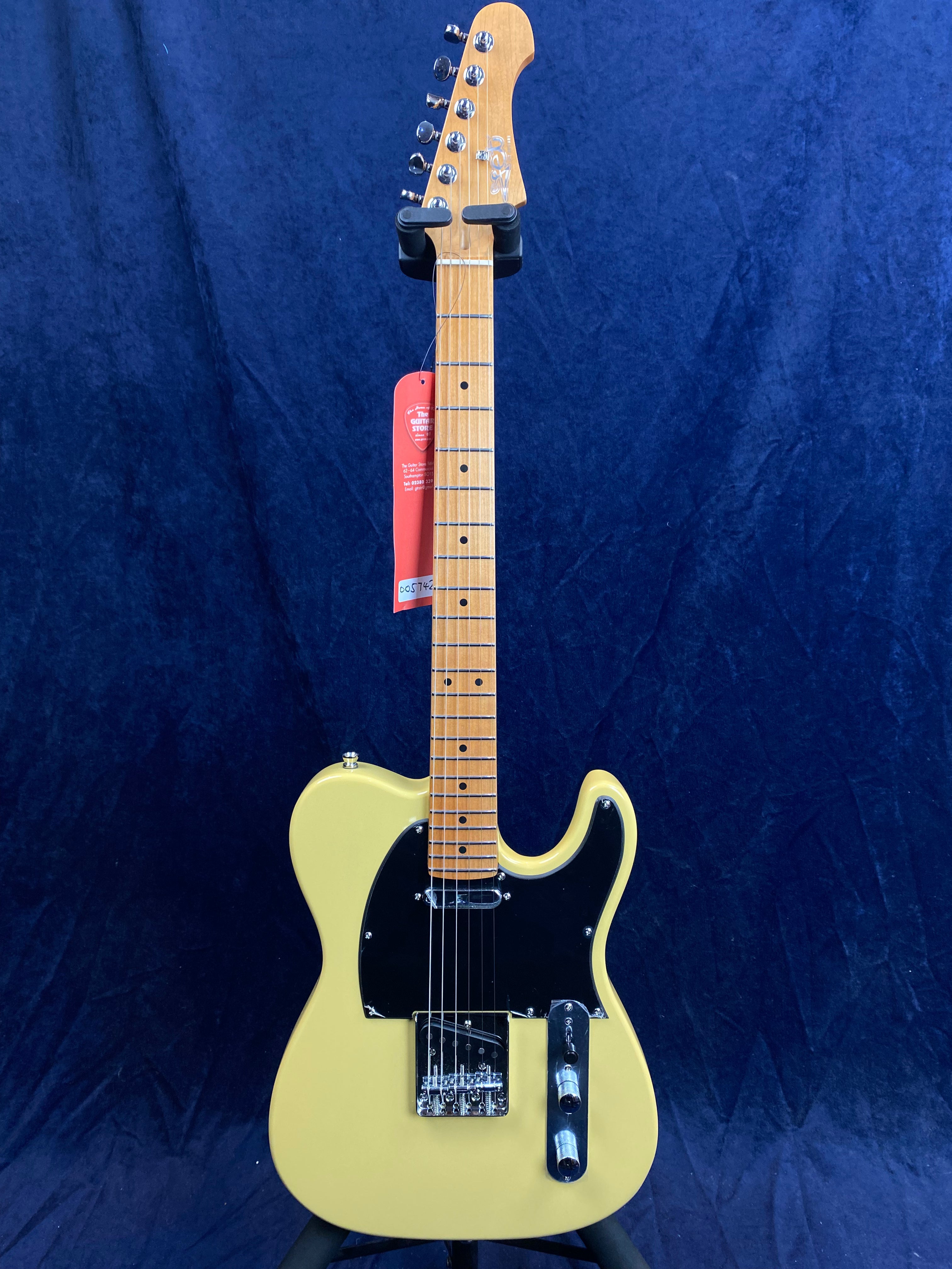 Yellow electric guitar with a black pickguard, chrome hardware, and a light wood neck, displayed on a stand against a dark blue background.
