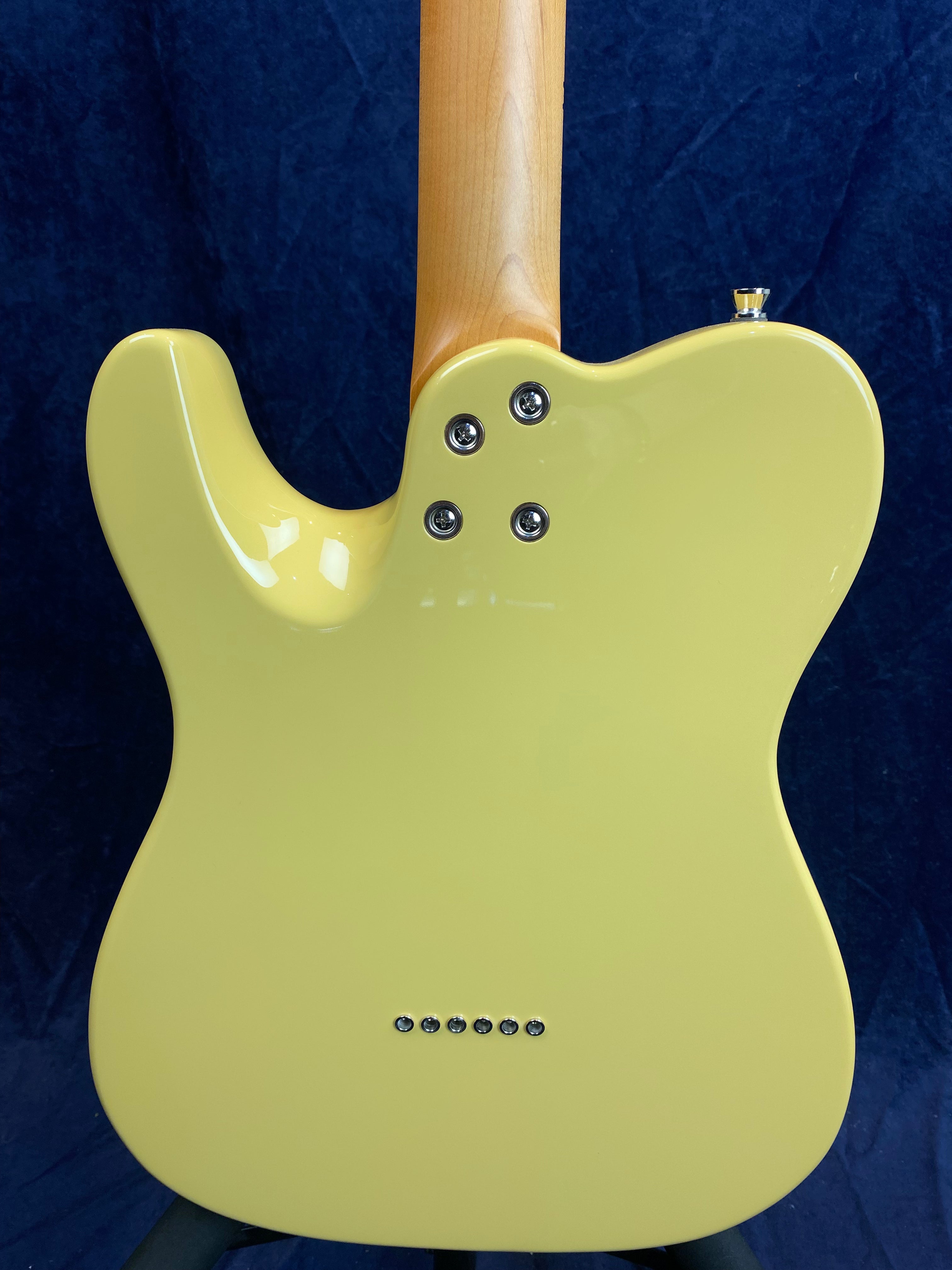 Back view of a yellow electric guitar with a natural wood neck, four neck bolts, and six metal string ferrules near the bottom.