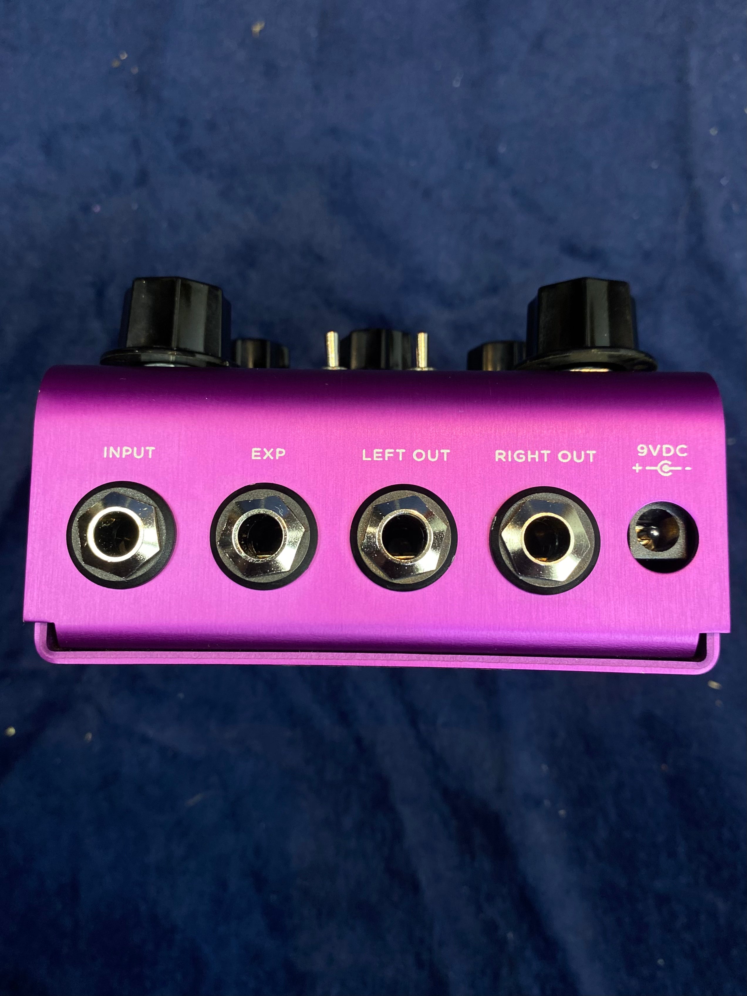 Purple FX pedal with four jacks labeled Input, EXP, Left Out, Right Out, and a 9VDC power port, all viewed from the top edge.
