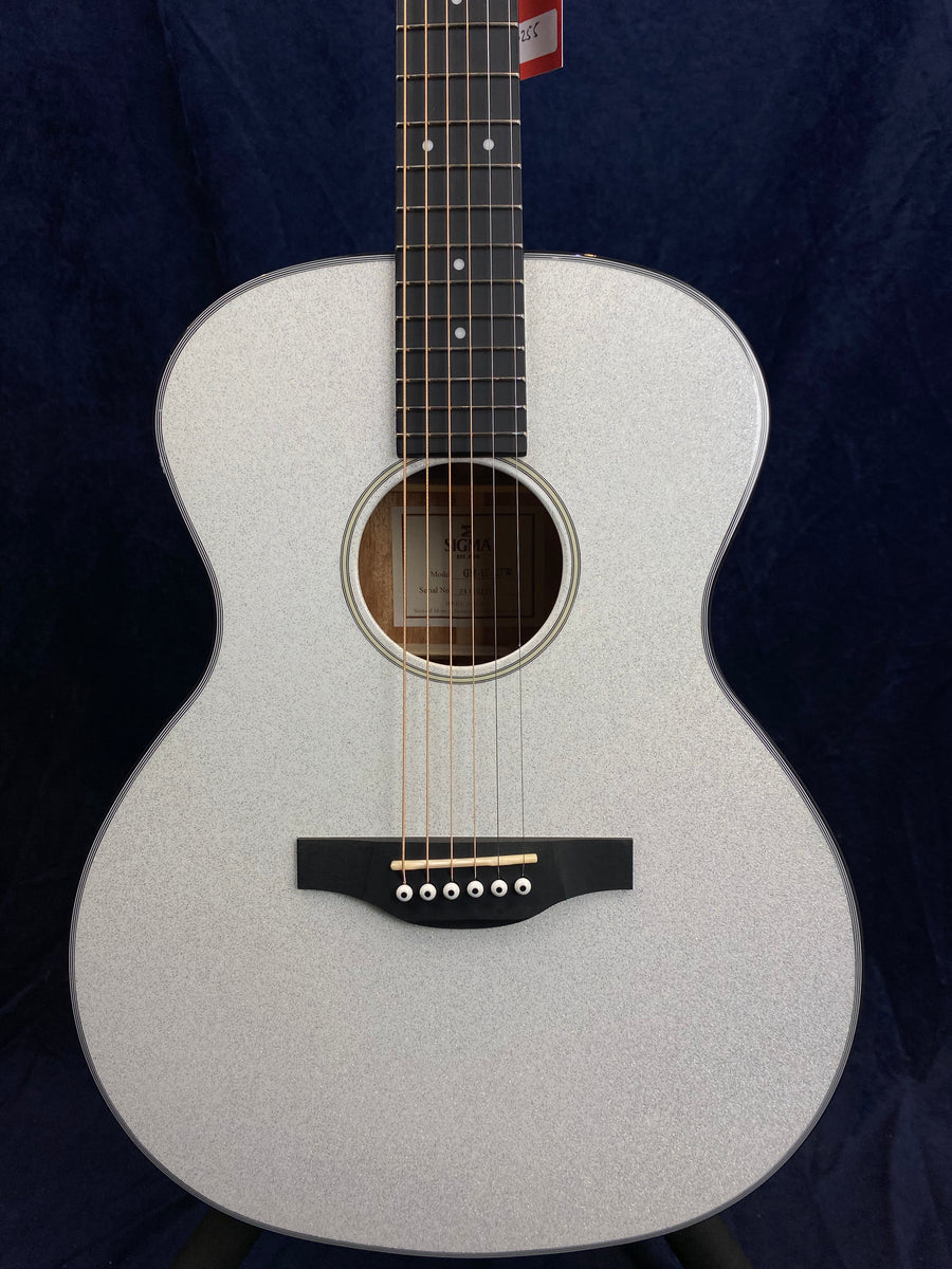Silver acoustic guitar with six strings, a dark bridge, and a circular sound hole, set against a dark background.