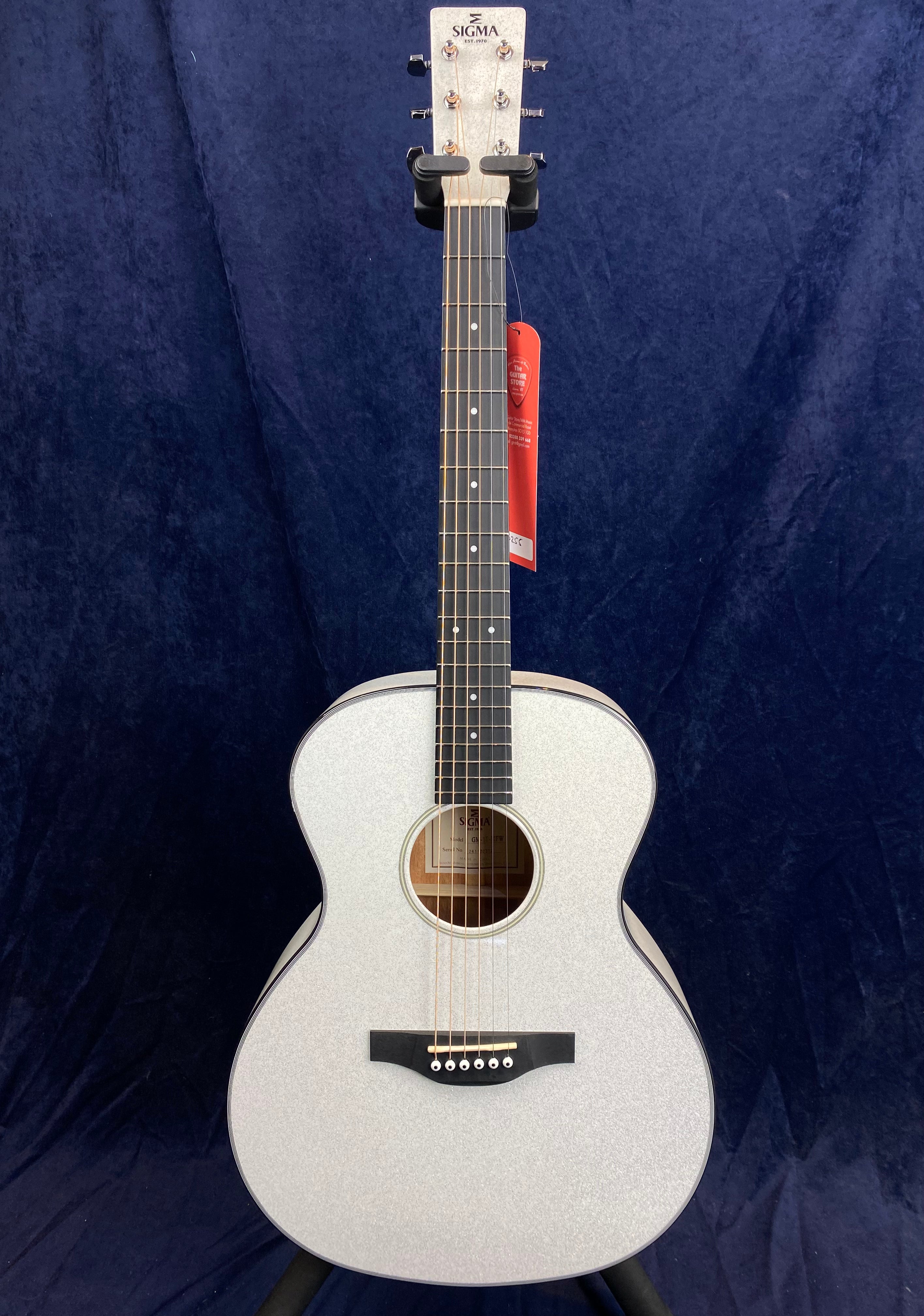 Sparkly silver Sigma acoustic guitar with a dark fretboard, round sound hole, and a red tag hanging from one tuning peg.